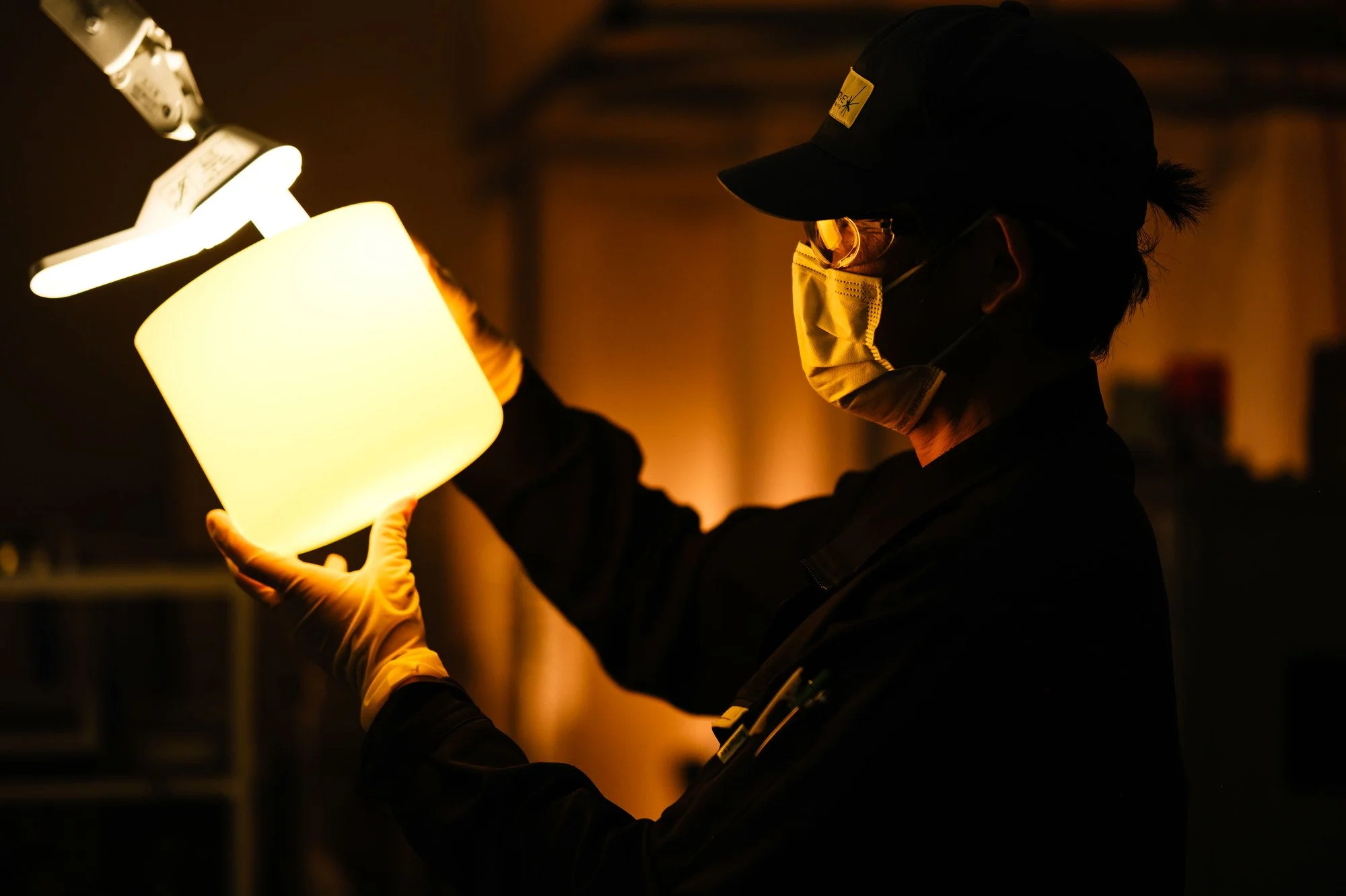 A worker carefully inspects finished quartz crucible under a lamp for quality control.