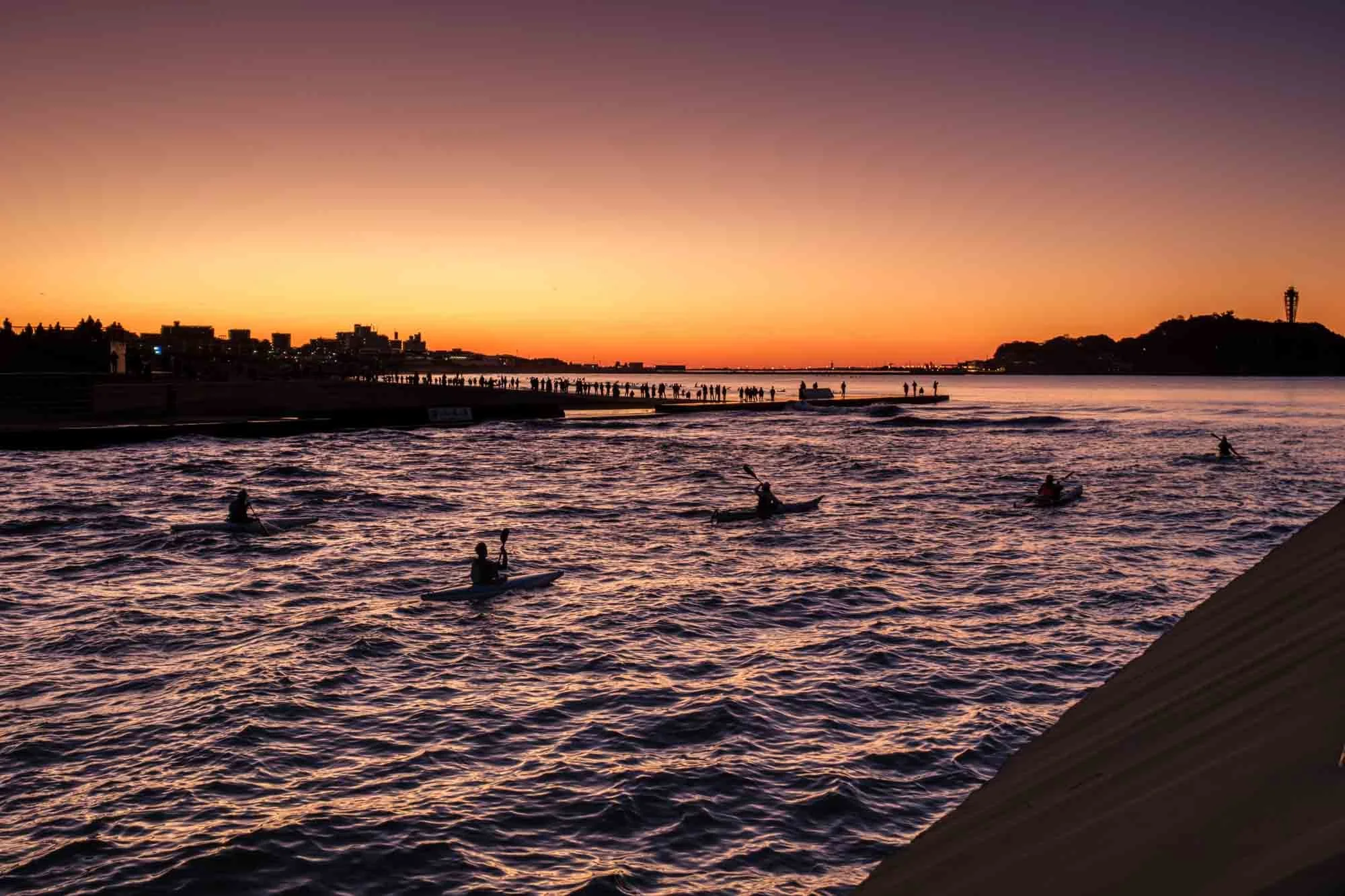 A group of sea kayakers paddle in the water as the sun rises.
