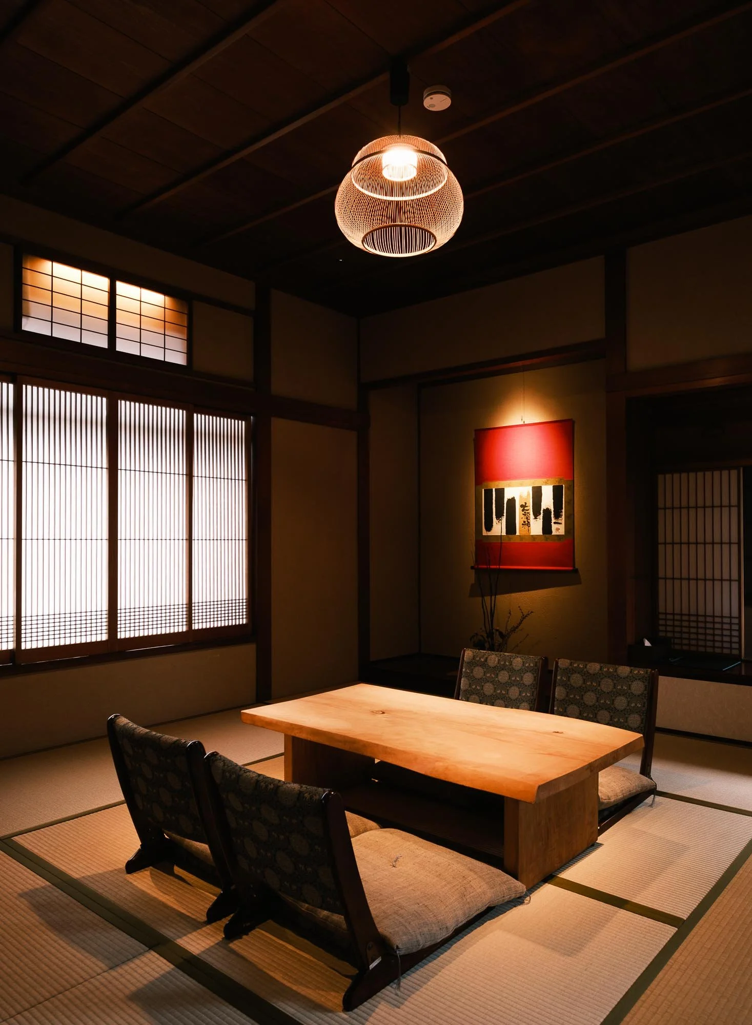 Interior of traditional Japanese tatami room with a low wooden table, four chairs with cand a red and black wall hanging.