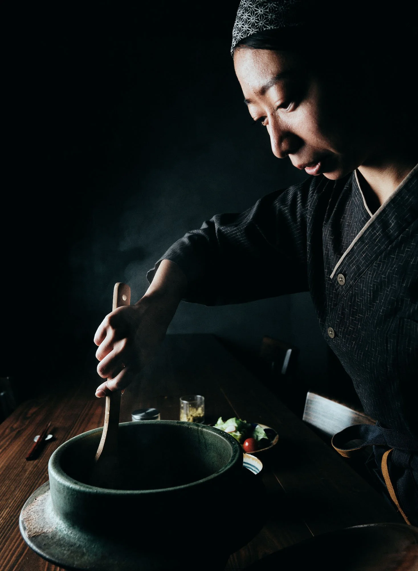A woman dressed in traditional Japanese attire cooking food in a dark setting.
