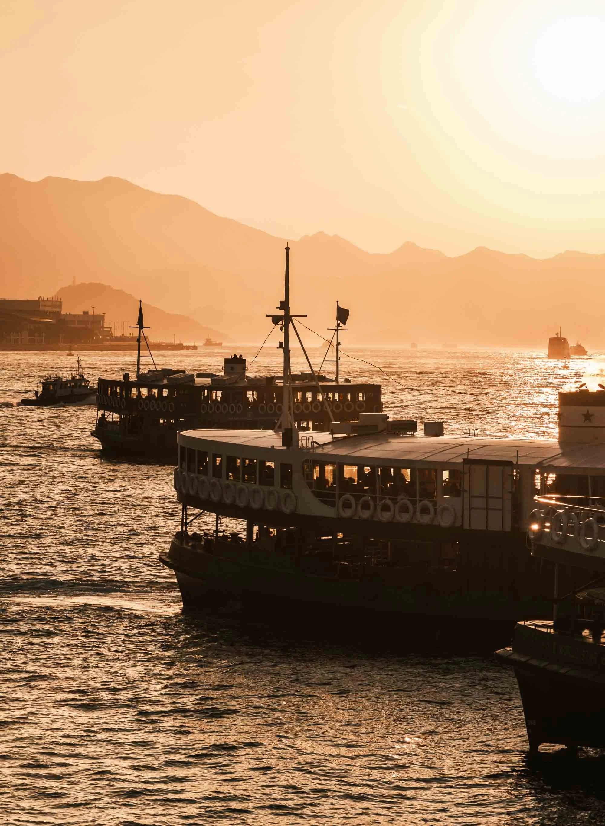 Ferries on water during sunset with mountains in the background.