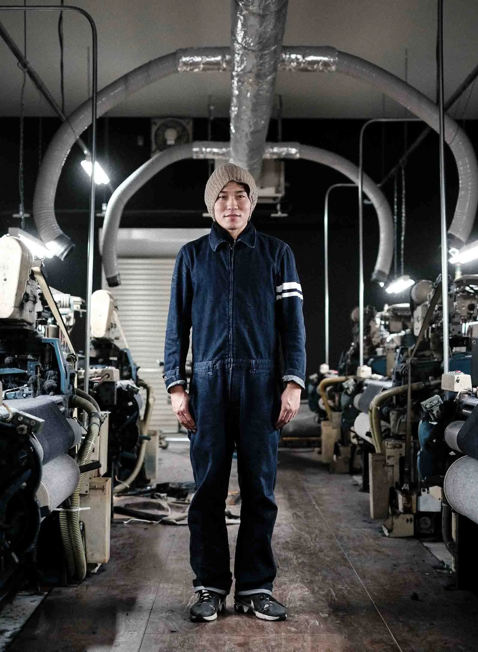 Portrait of textile worker in a workshop surrounded by denim weaving looms.