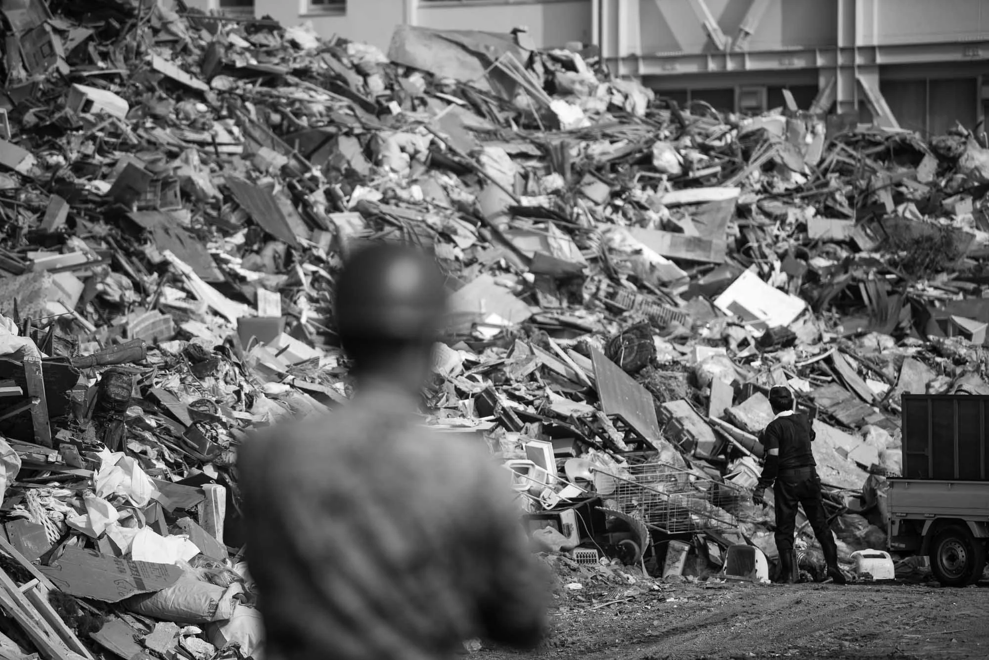 Person standing next to a large pile of debris and trash, with another person blurred in the foreground.