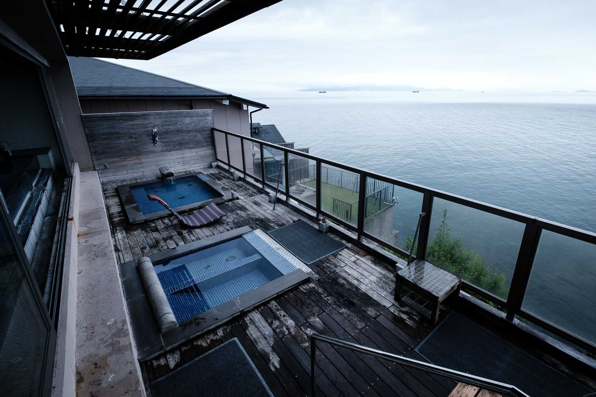 A balcony with two small hot tubs overlooking the sea with ships in the distance.
