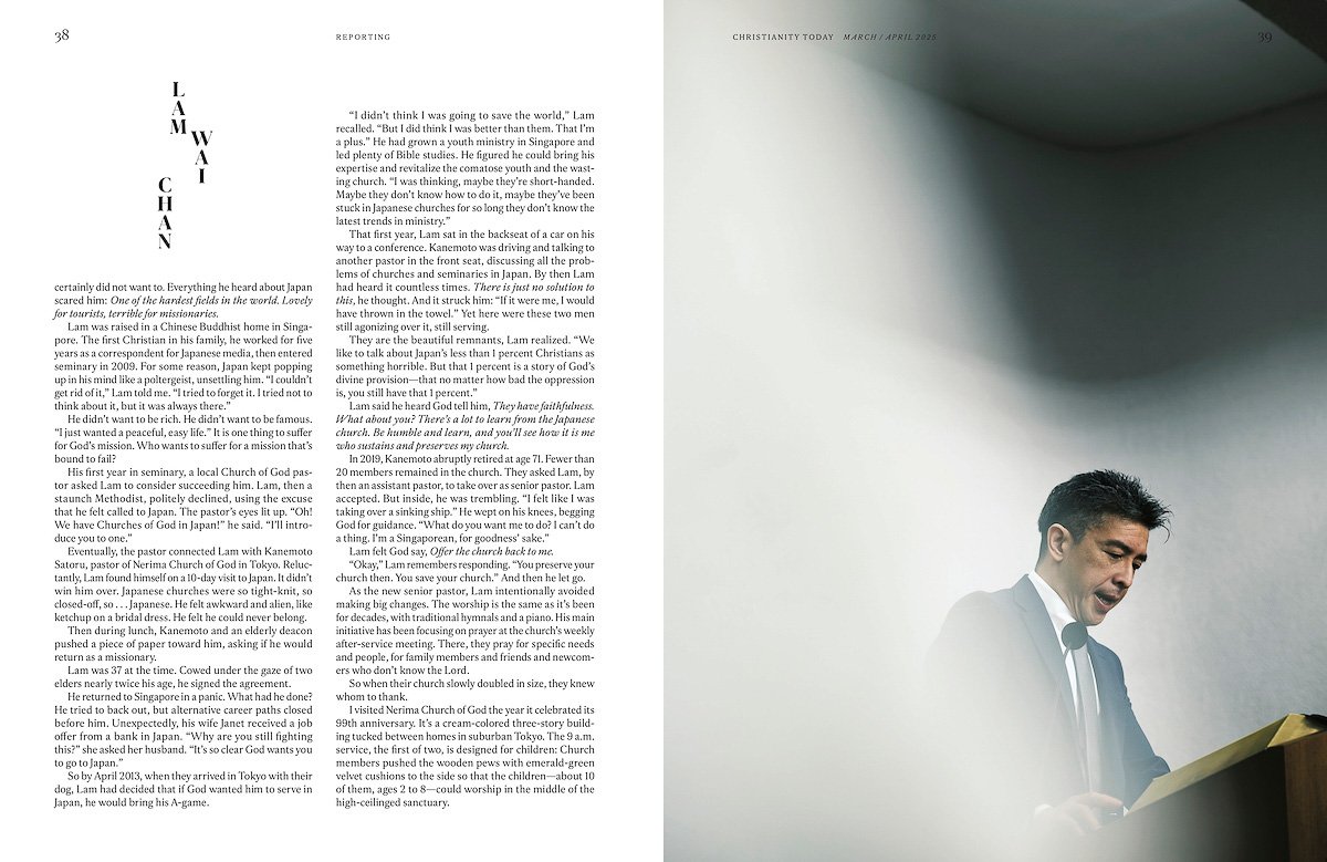 A man in a suit reading a book at a podium during a service or event, with a large window and cloudy sky in the background.