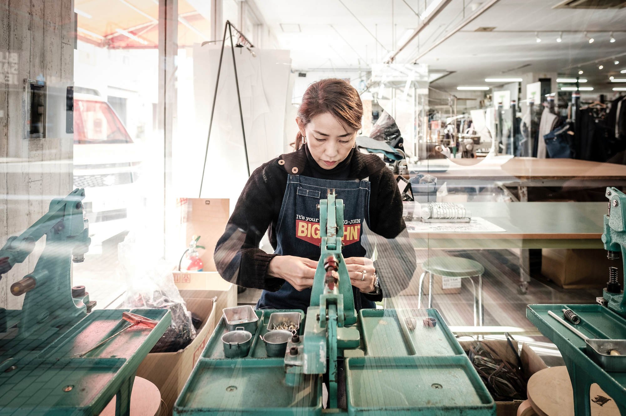 Worker operating industrial textile machine in a jeans and denim fashion shop in Japan.