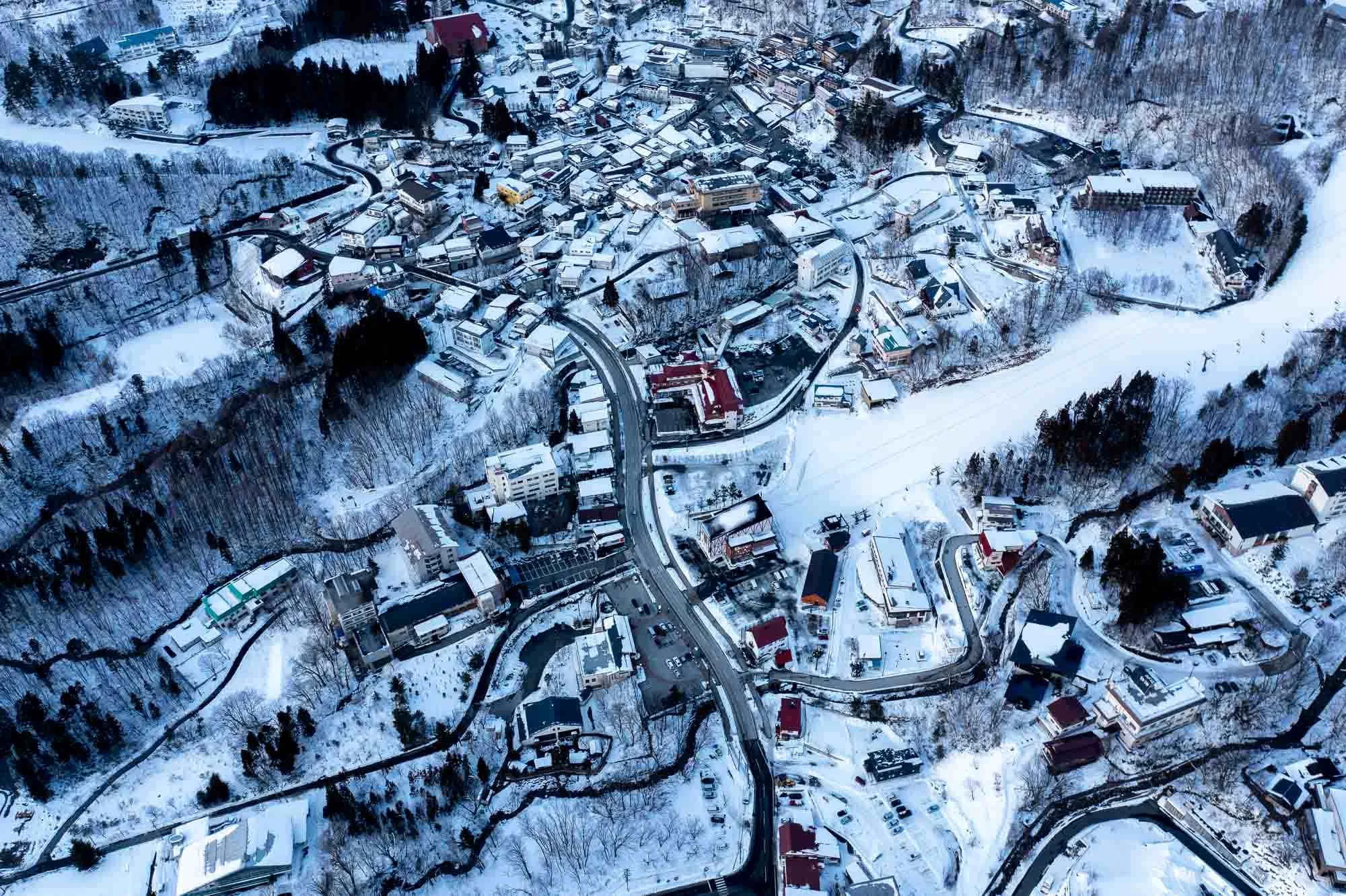 Aerial view of a snow-covered town with winding streets and houses, Japan travel photography by Ben Weller.