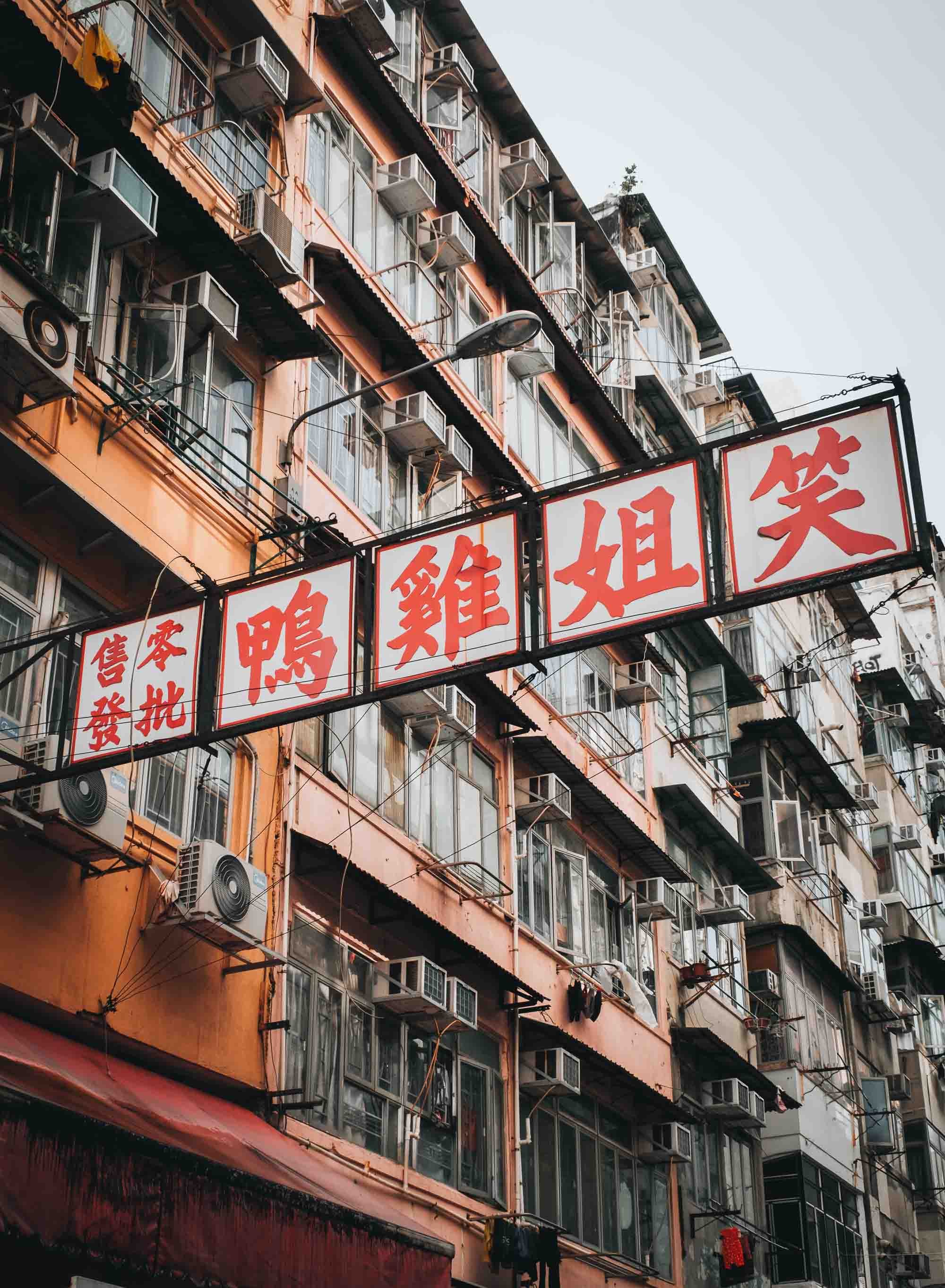 A Hong Kong apartment building with numerous windows, air conditioning units, and signs with Chinese characters in red. 