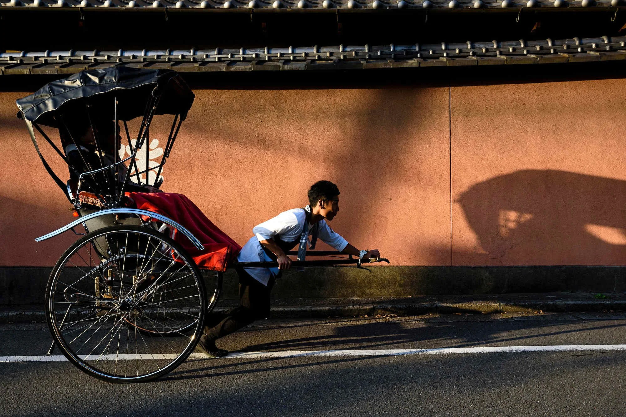 Traditional rickshaw puller transporting passenger through historic street in Kyoto.
