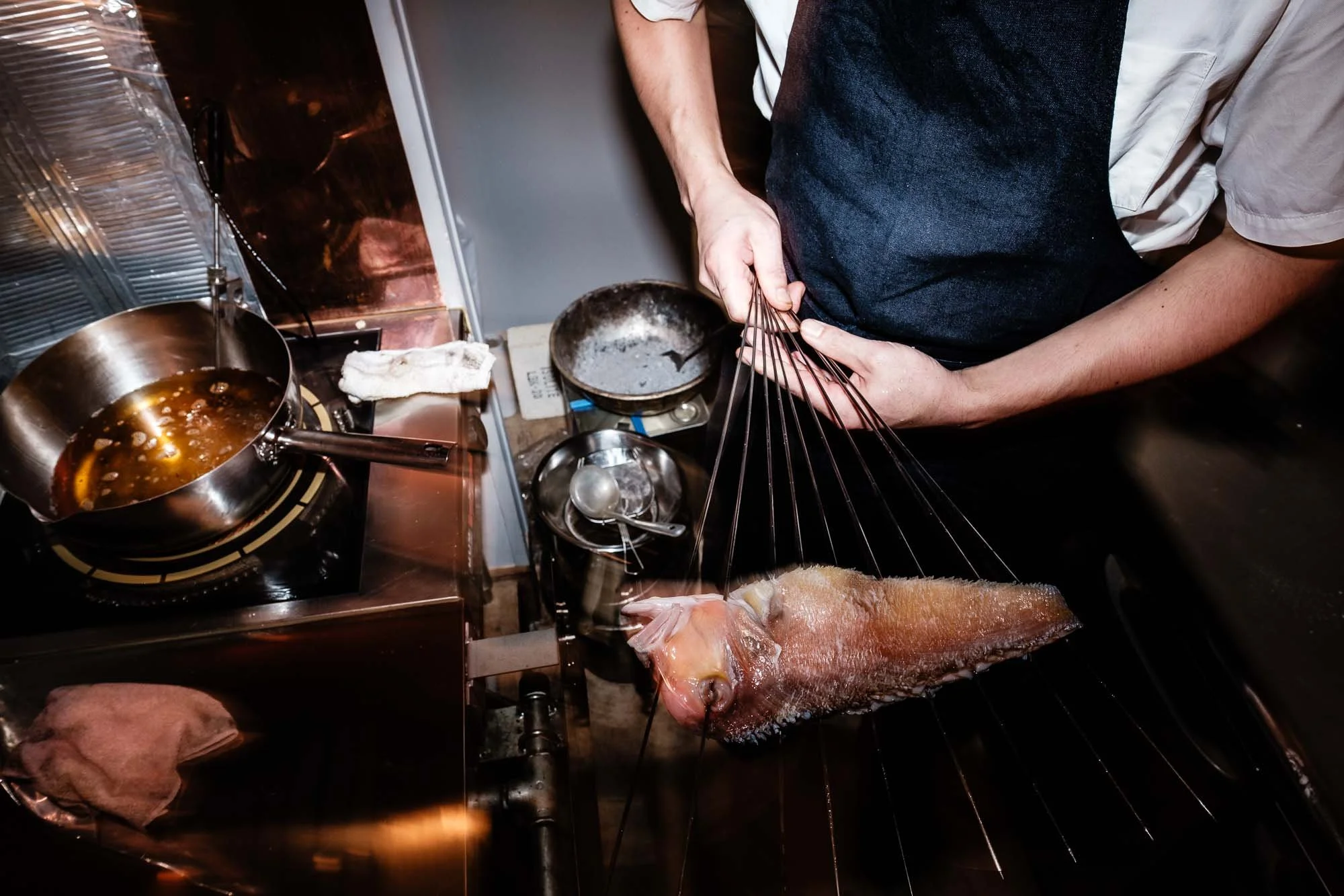 A chef skewering a whole fish on a grill for cooking in a professional kitchen.