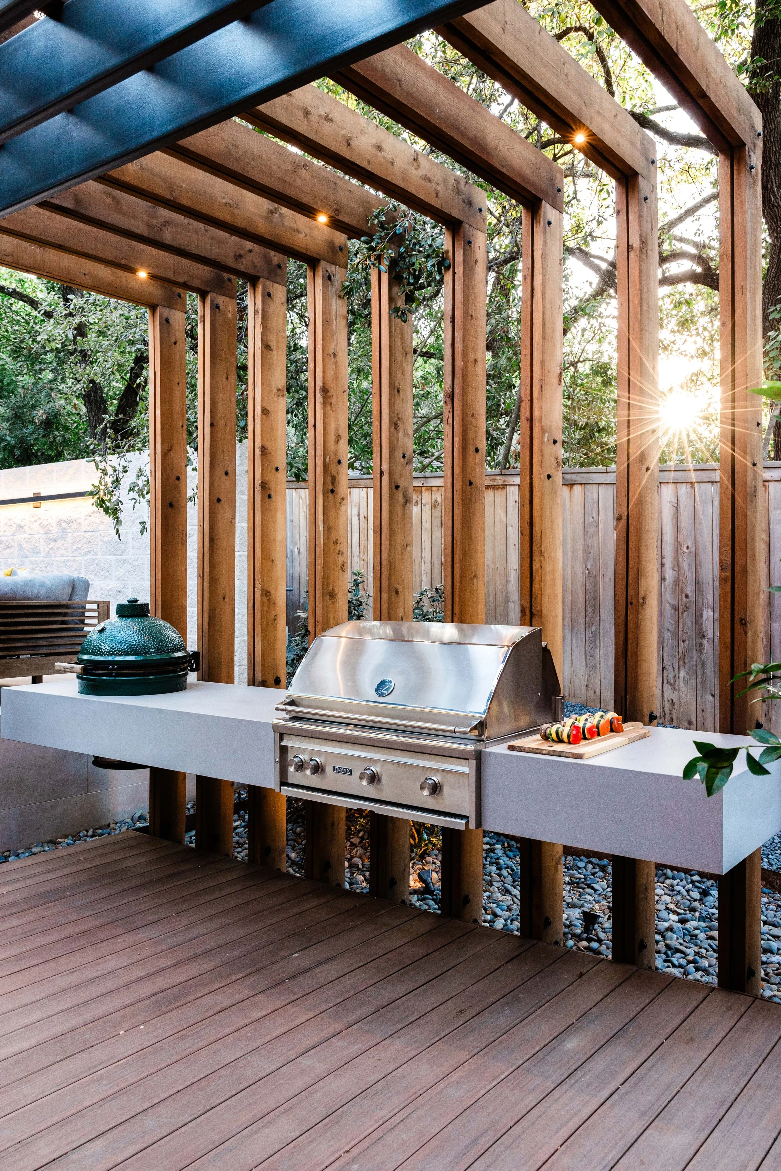 Modern outdoor kitchen with grill and Big Green Egg smoker framed by wood and steel privacy screen