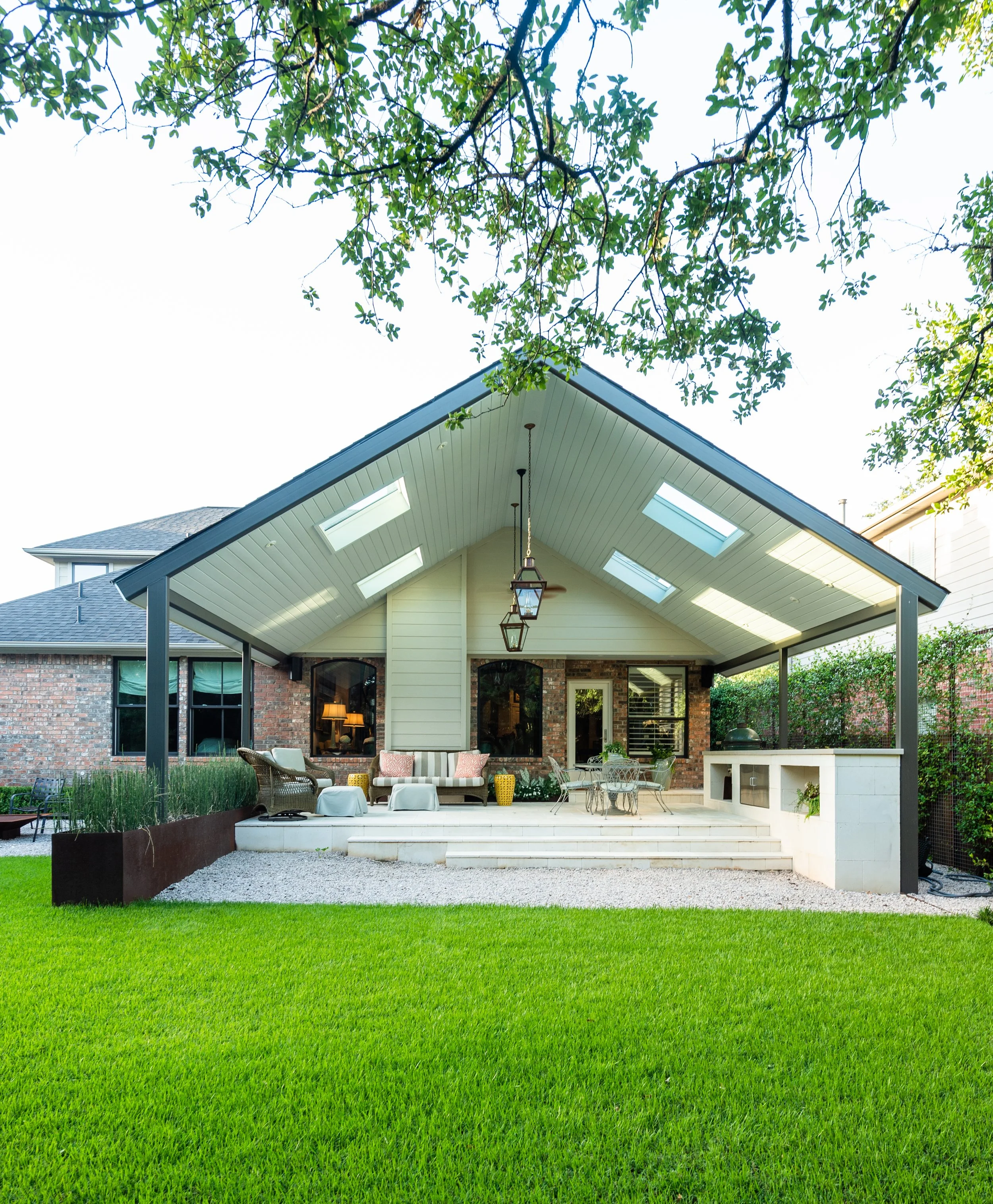 Vaulted patio roof with skylights shelters an outdoor kitchen and lounge off the backyard