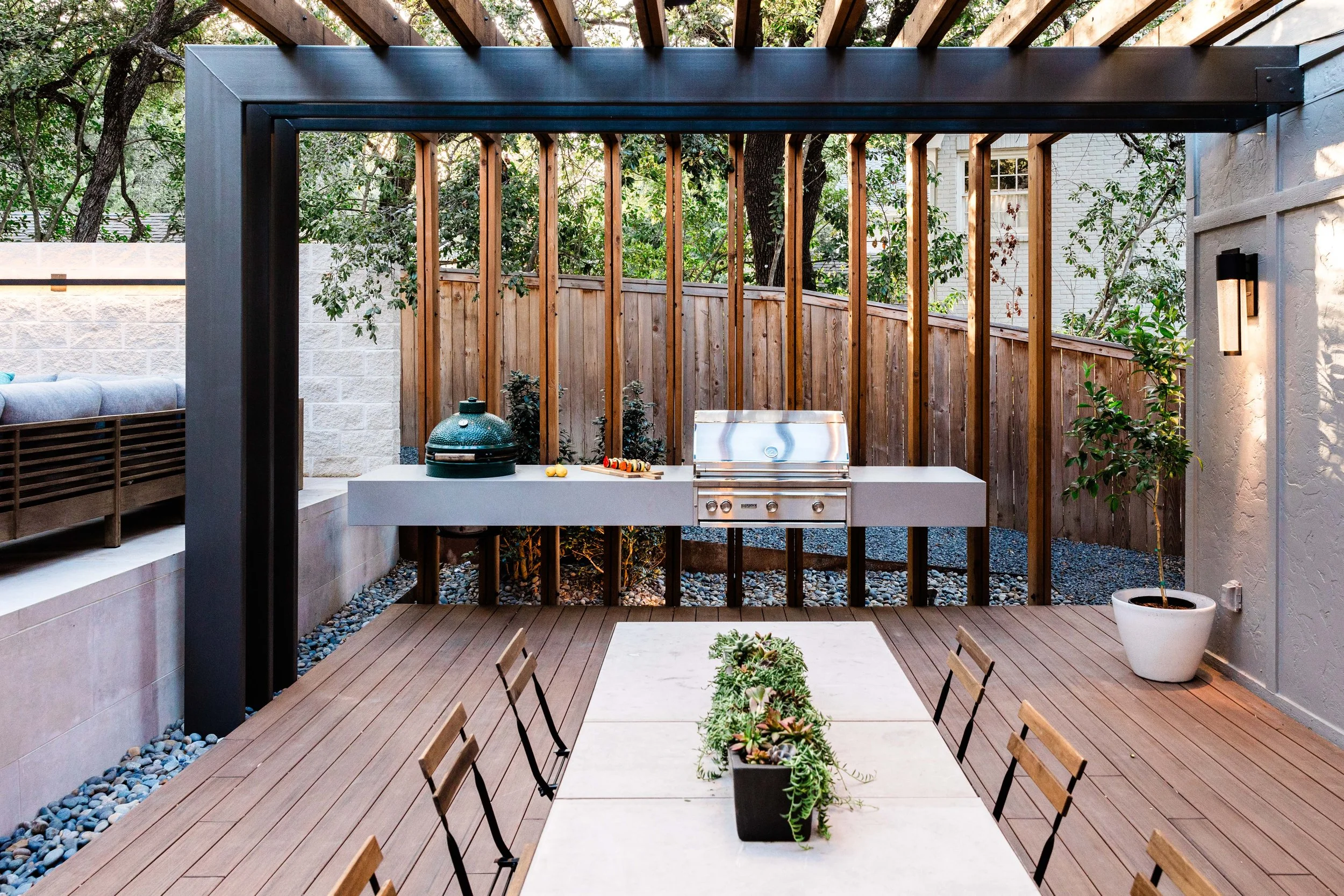 A modern porcelain grilling area with stainless steel appliances and a Big Green Egg, surrounded by a steel-framed pergola and vertical cedar screen for privacy