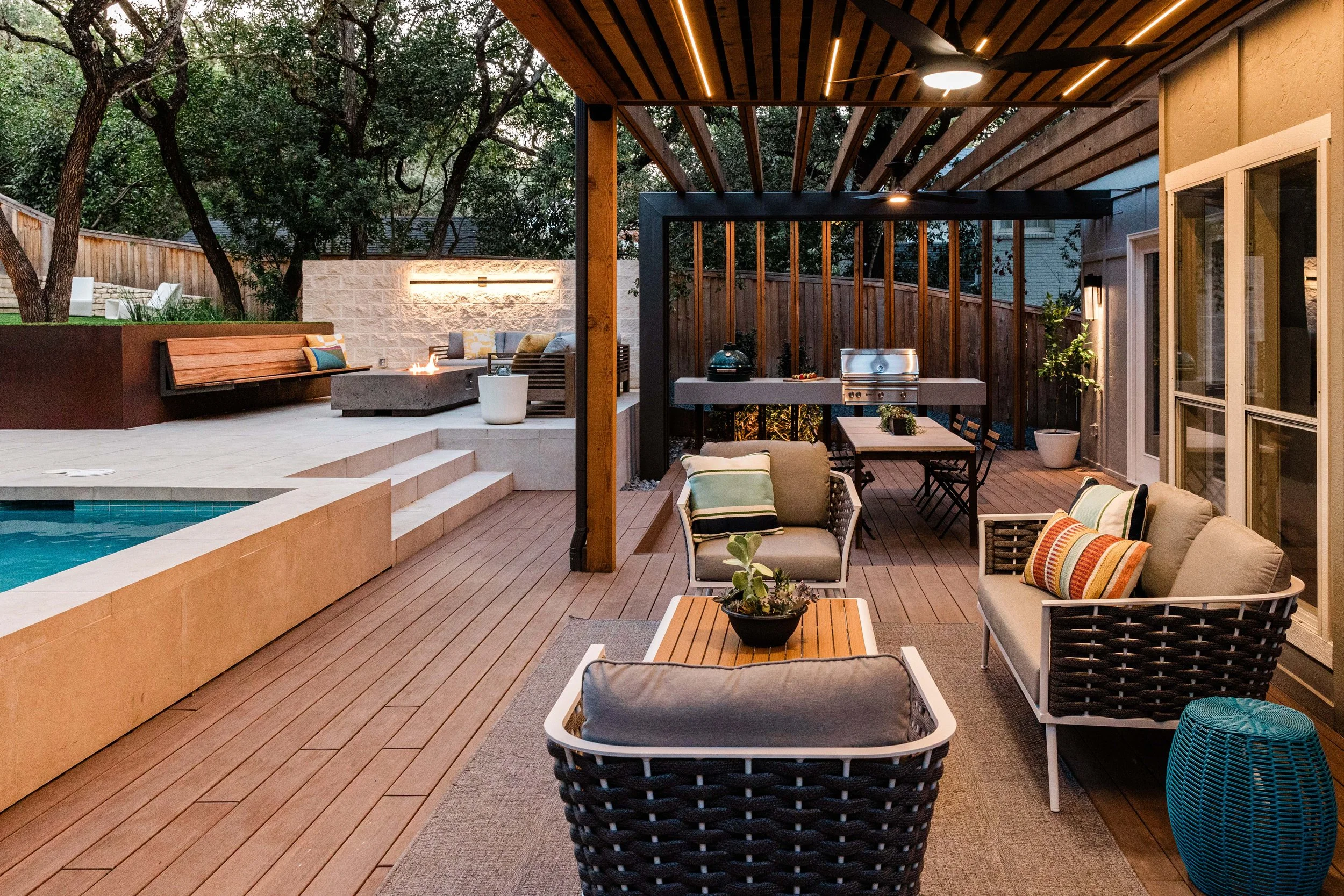 A twilight shot of the same deck showing ambient lighting under the pergola, with warm tones bringing out the textures of the wood and cushions