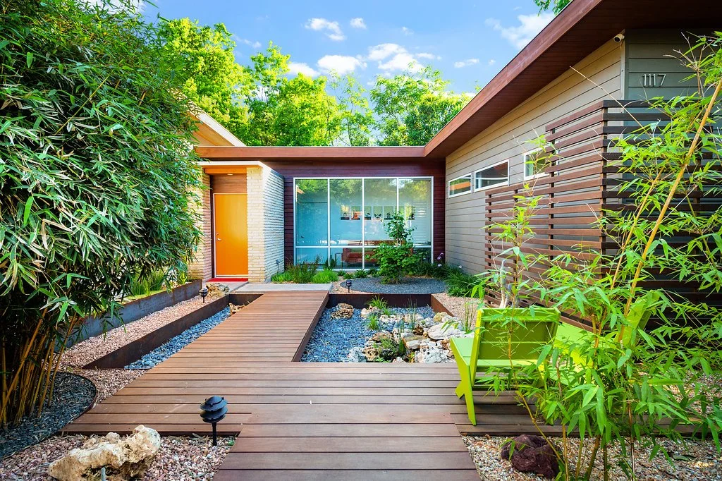 Modern house with outdoor wooden deck and garden, green plants, and a bright green chair on the patio.