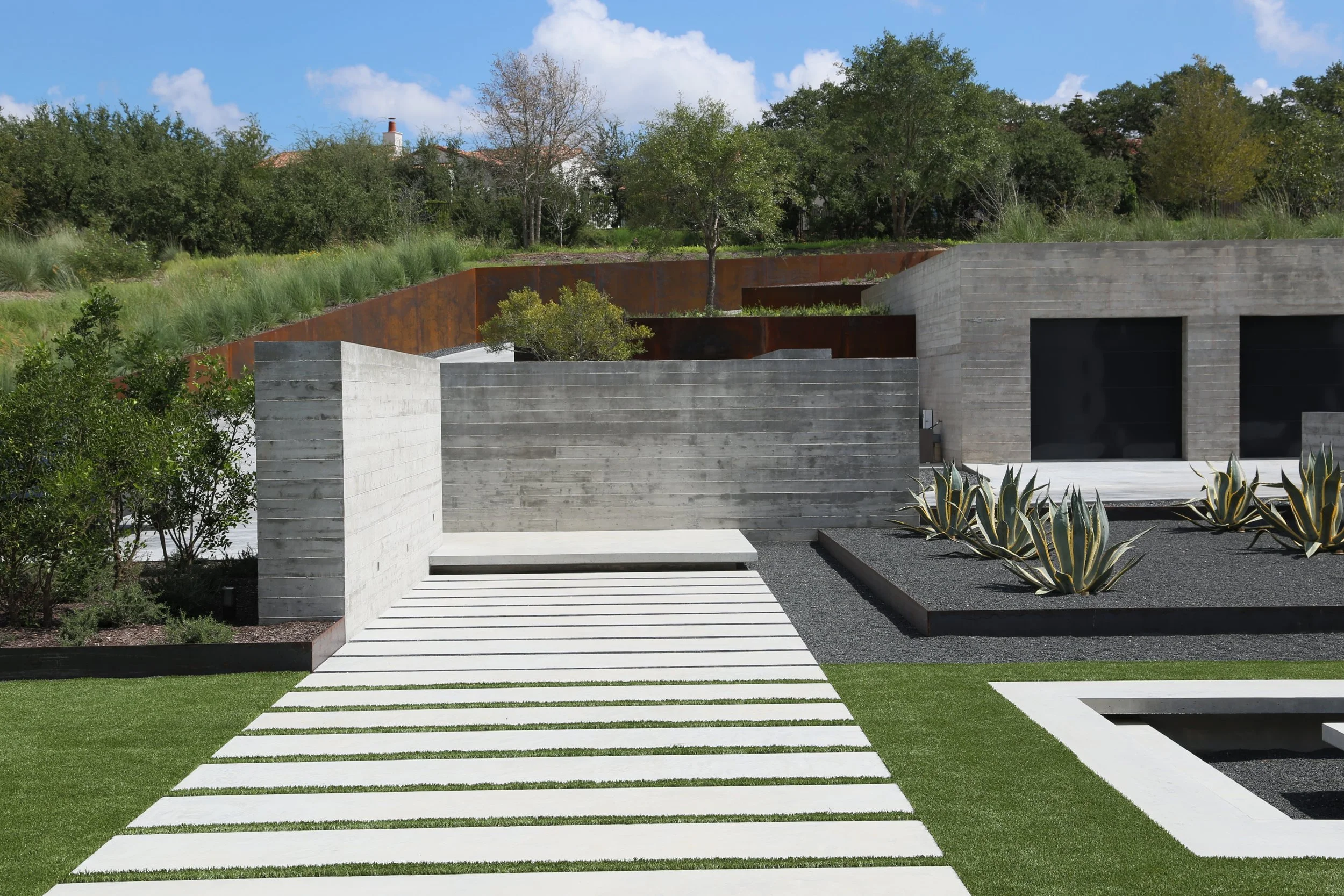 Modern hillside courtyard featuring a stepped concrete walkway, agave-lined beds, and rusted steel retaining walls—blending sculpted geometry with native slope