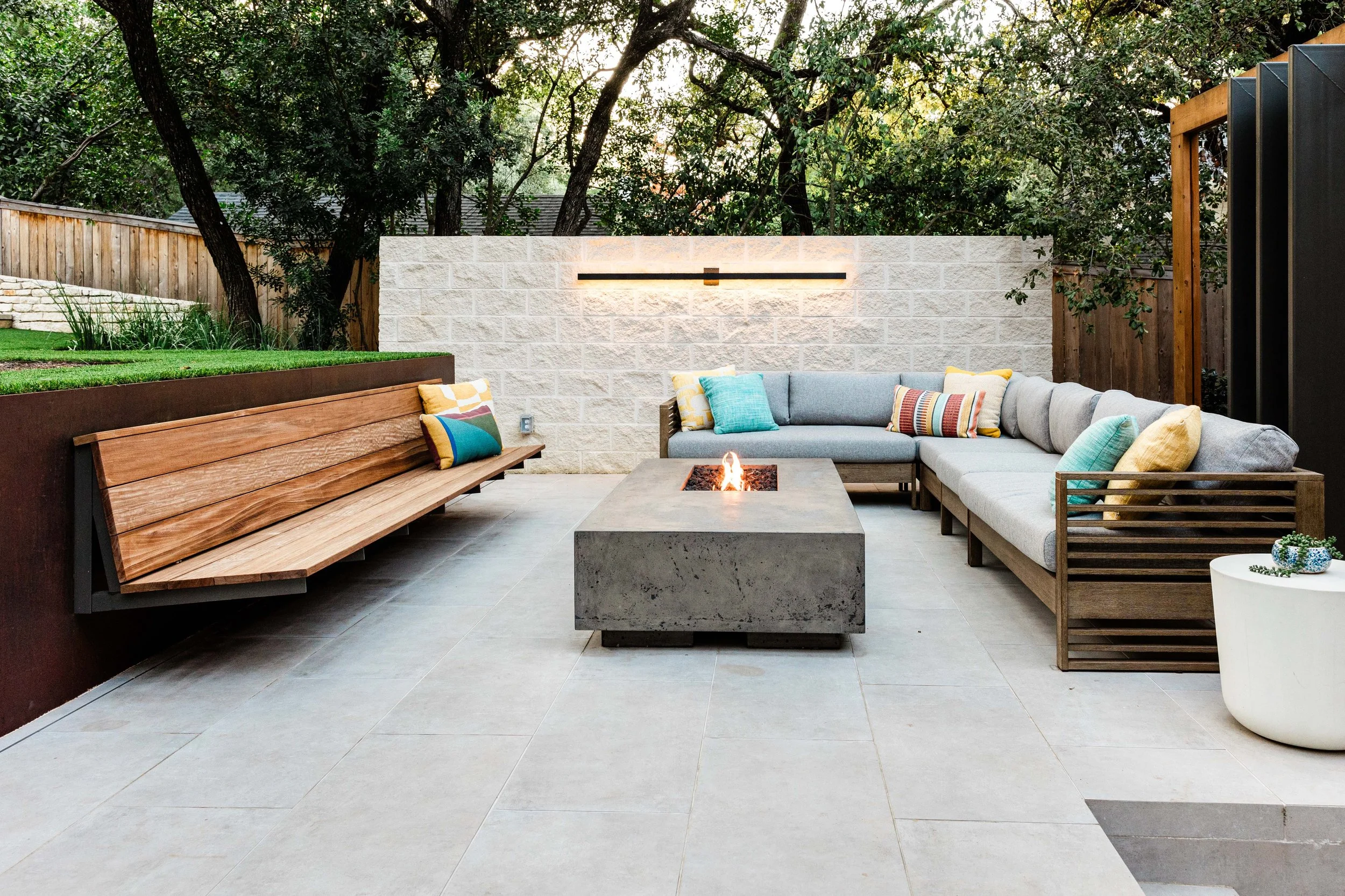 Contemporary fire pit lounge with ipe bench seating and illuminated limestone wall backdrop