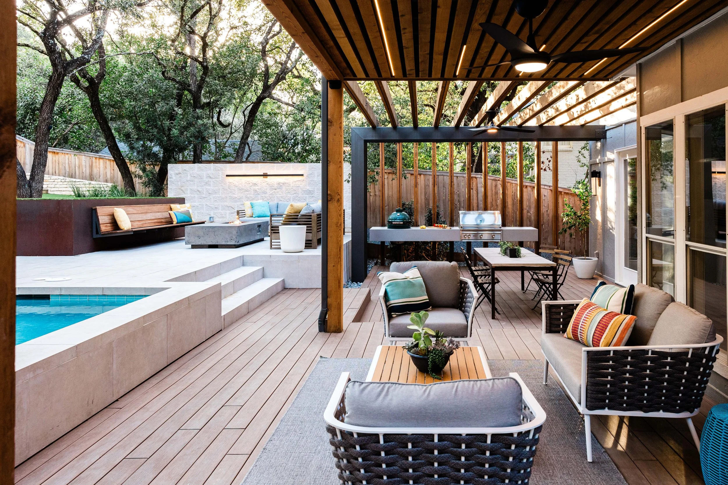 A view from the deck highlighting a shaded lounge area, grill station, and sunken seating around the pool, blending indoor comfort with outdoor style