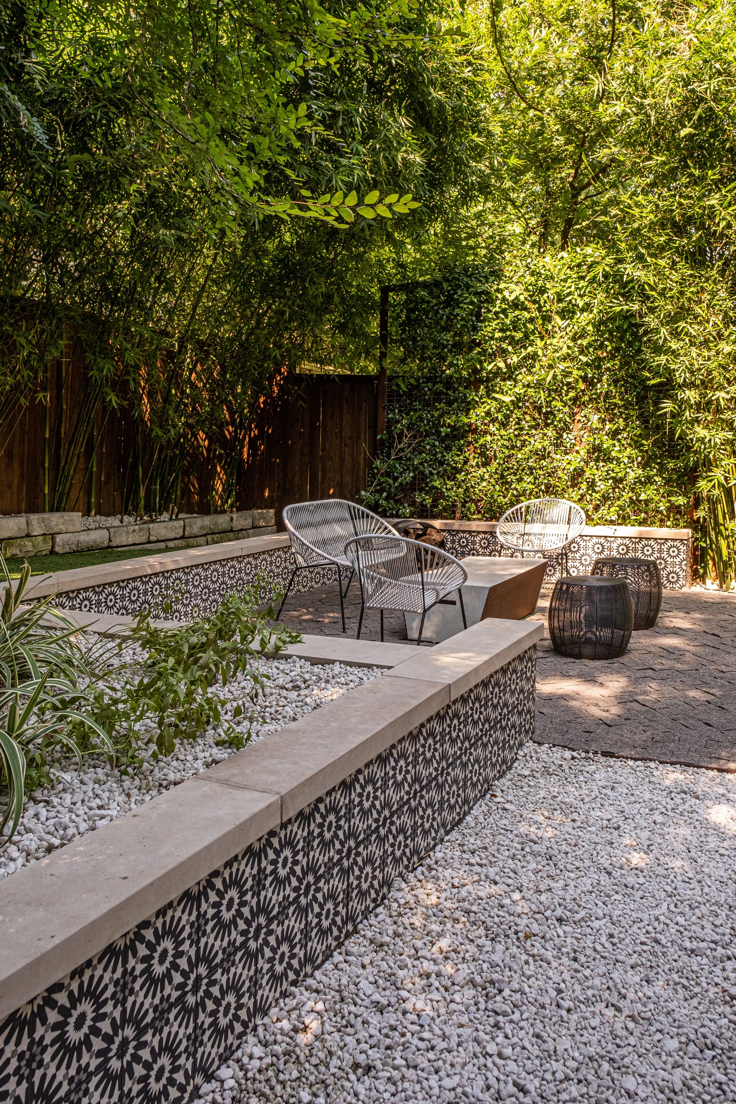 Patterned tile seating wall and fire pit lounge surrounded by bamboo and gravel garden in a quiet backyard retreat