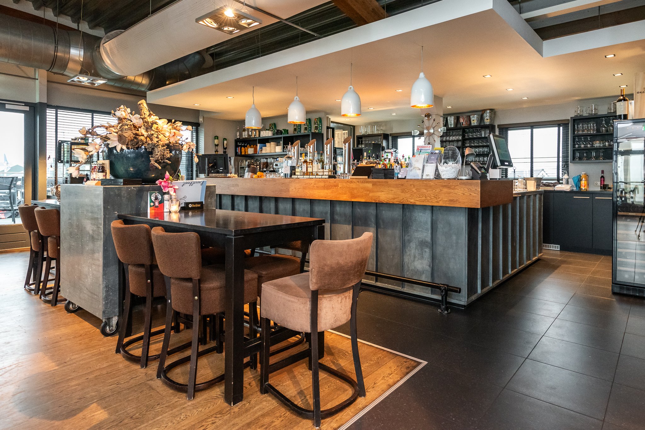 Interieur van
met een bar en zithoeken, decoratief bloemstuk op tafel, hanglampen en grote ramen.
