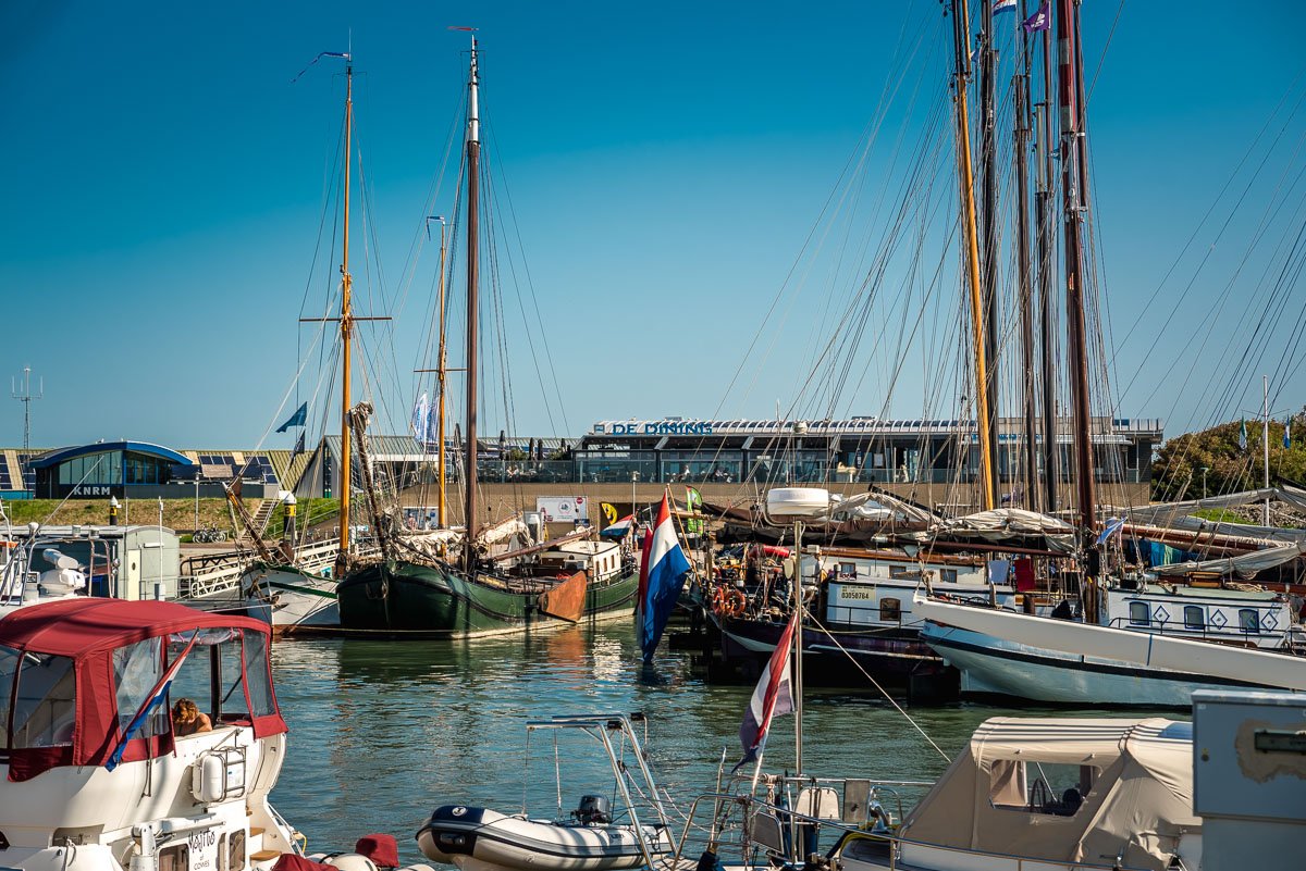 Meerboten en schepen in een haven van Vlieland met een modern gebouw op de achtergrond