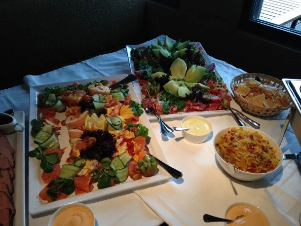 Buffet met diverse salades en verse groente, inclusief gesneden fruit, groenten en aardappelgebaseerde gerechten.
