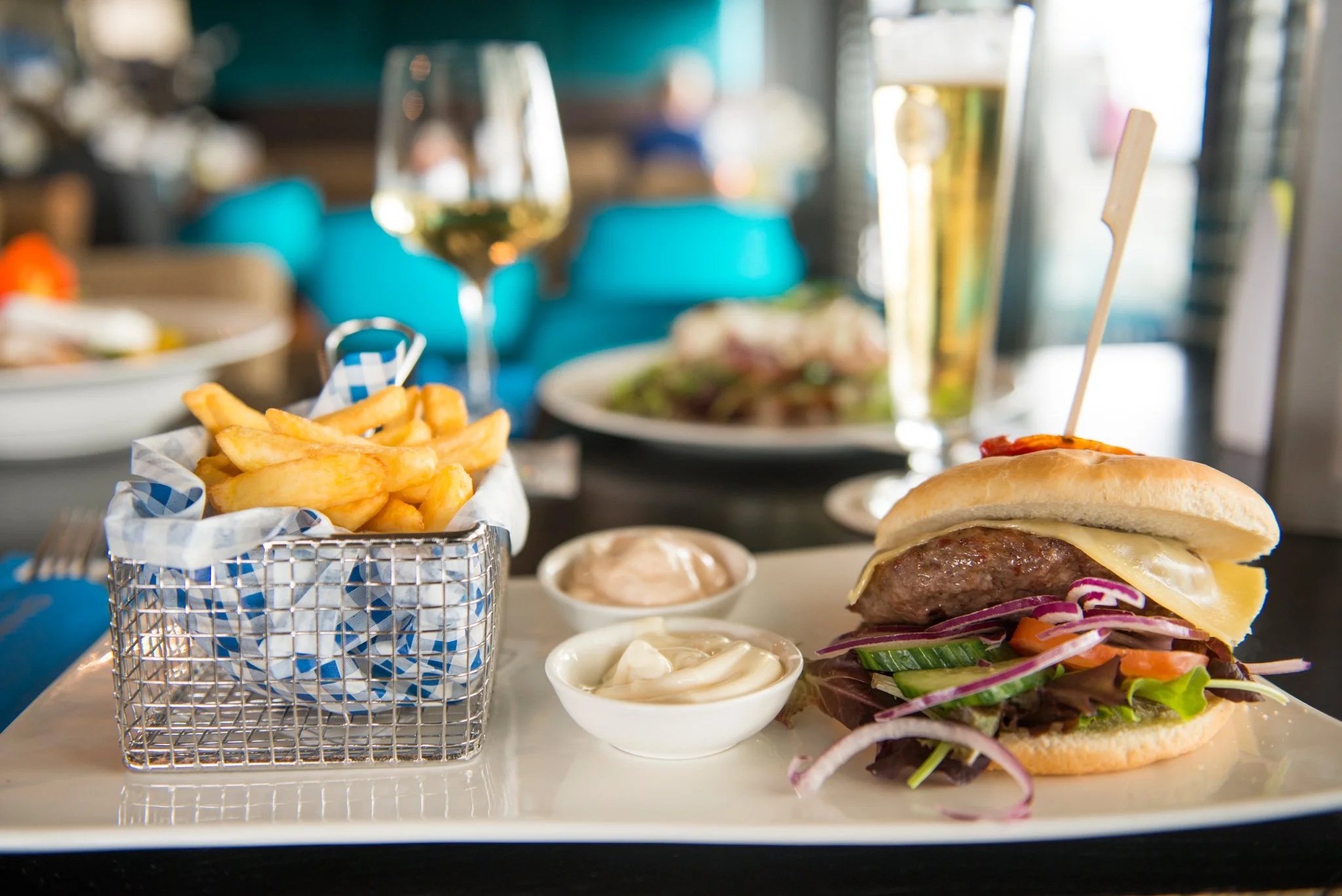 Hamburger met groenten en kaas, Franse frieten, twee sauzen, een glas witte wijn, en een glas bier op een restauranttafel van De Dining op Vlieland.