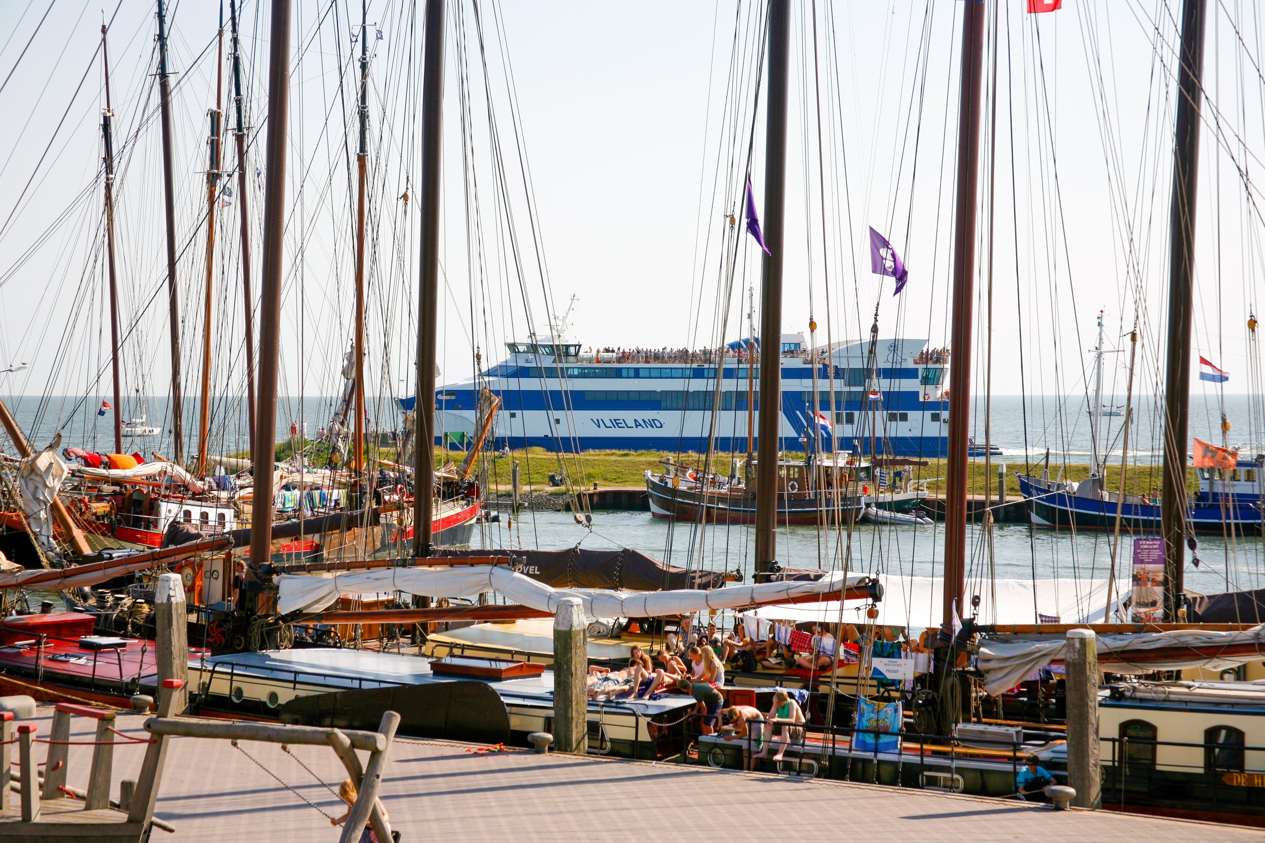 De haven van Vlieland met verschillende zeilboten en een grote blauw en witte veerboot op de achtergrond.