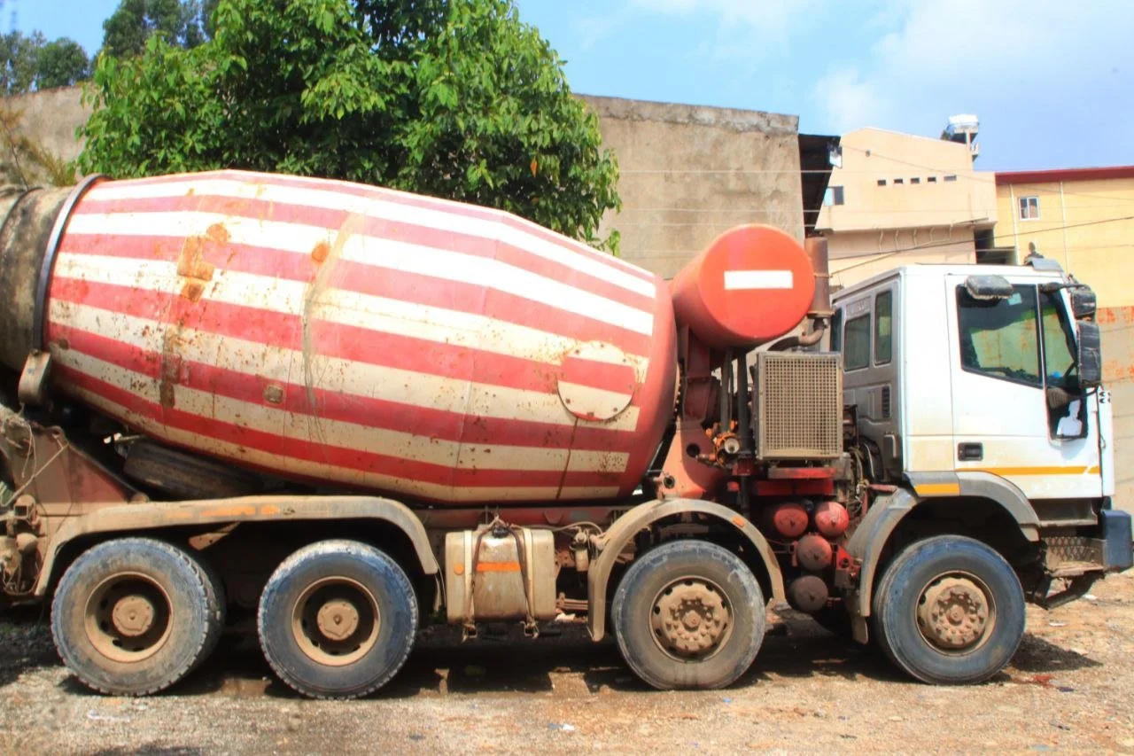 A concrete mixer truck with a red and white striped drum parked on a dirt surface.