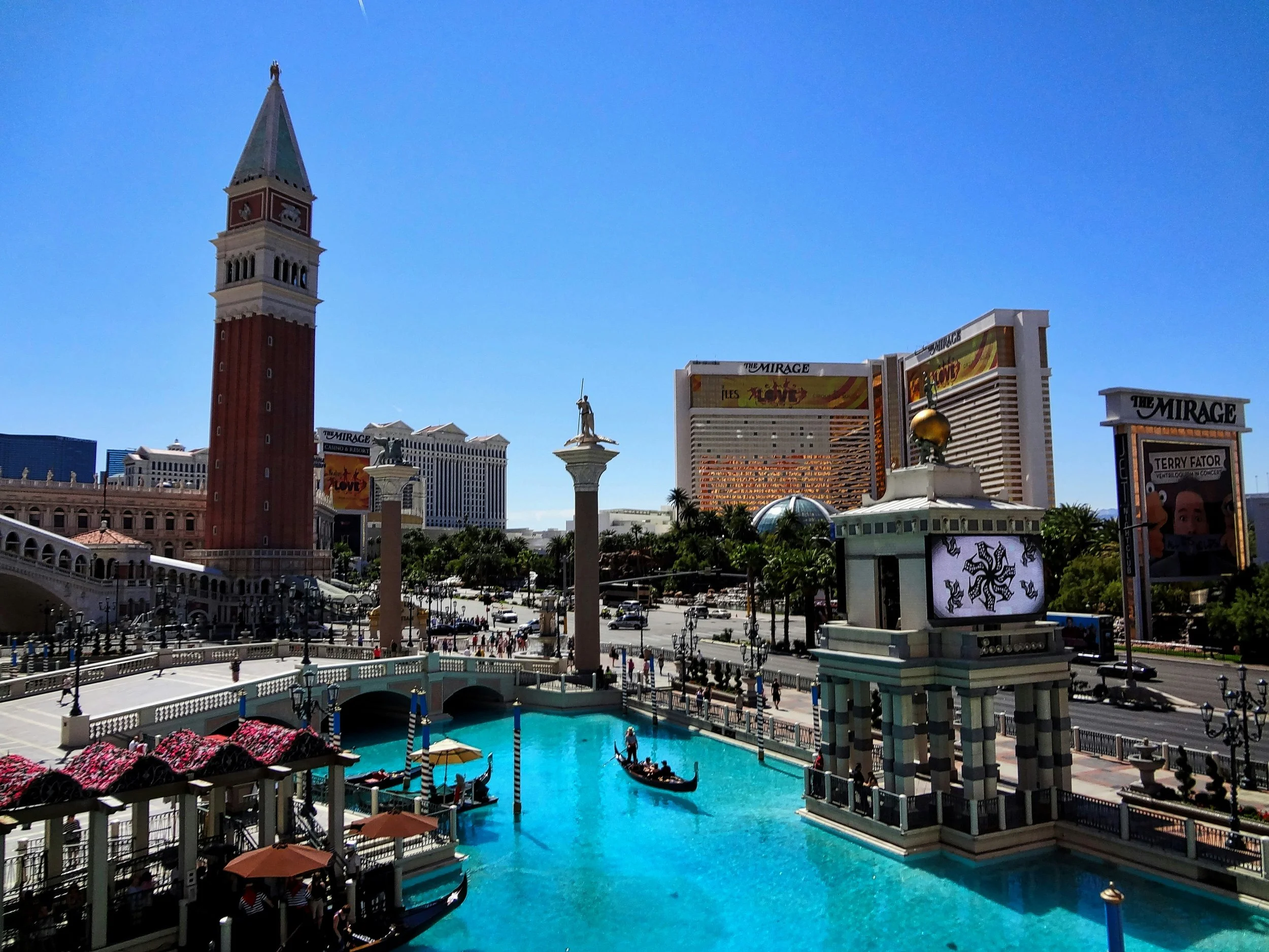 Vue de Las Vegas avec la tour de l'hôtel Venetian et le canal avec des gondoles, des colonnes, des statues et des buildings en arrière-plan.