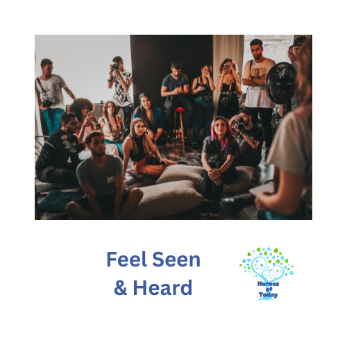 Group of people sitting on the floor and standing, listening to a person speaking in front of them during a workshop or seminar.