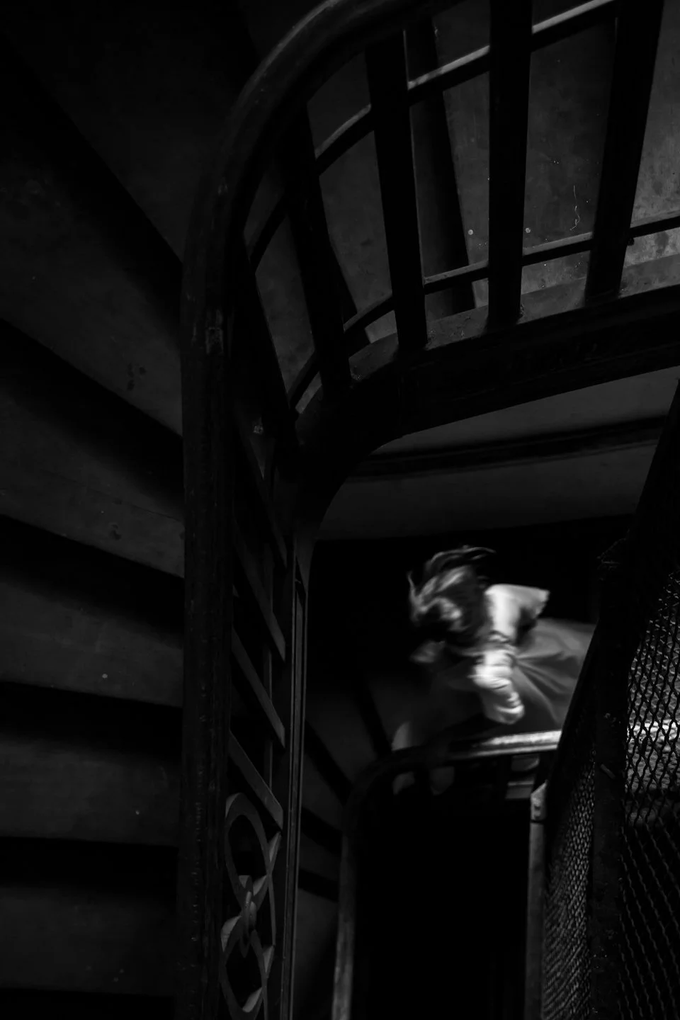 Black and white photo of a winding staircase with a child moving down the stairs.