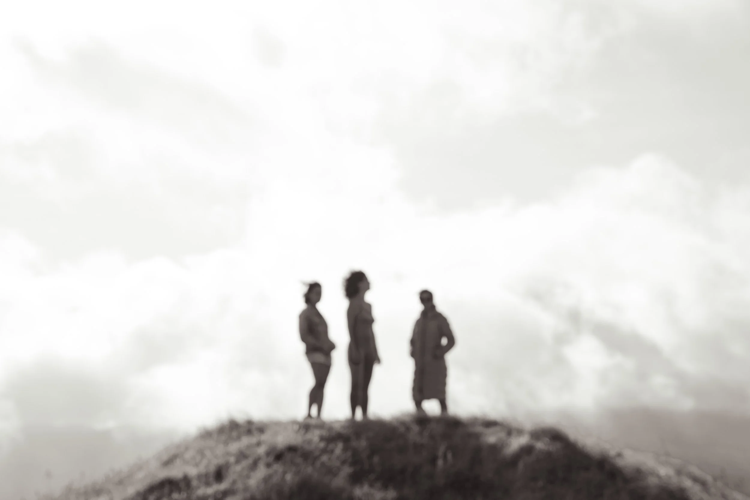 Four people together on top of a hill, against a cloudy sky, with a rough ground surface in the foreground.