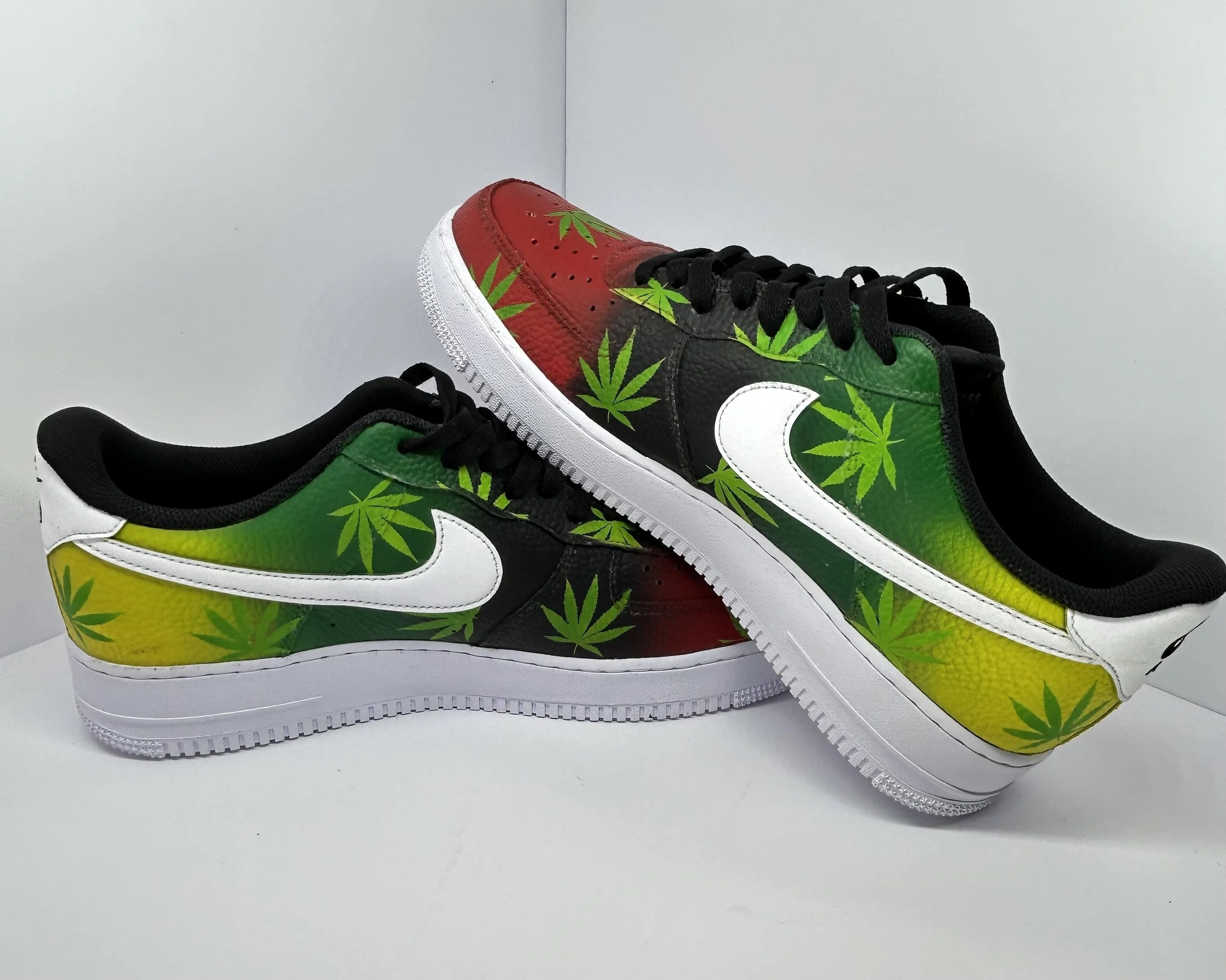 Pair of Nike sneakers with marijuana leaf designs in green, yellow, red, and black colors.