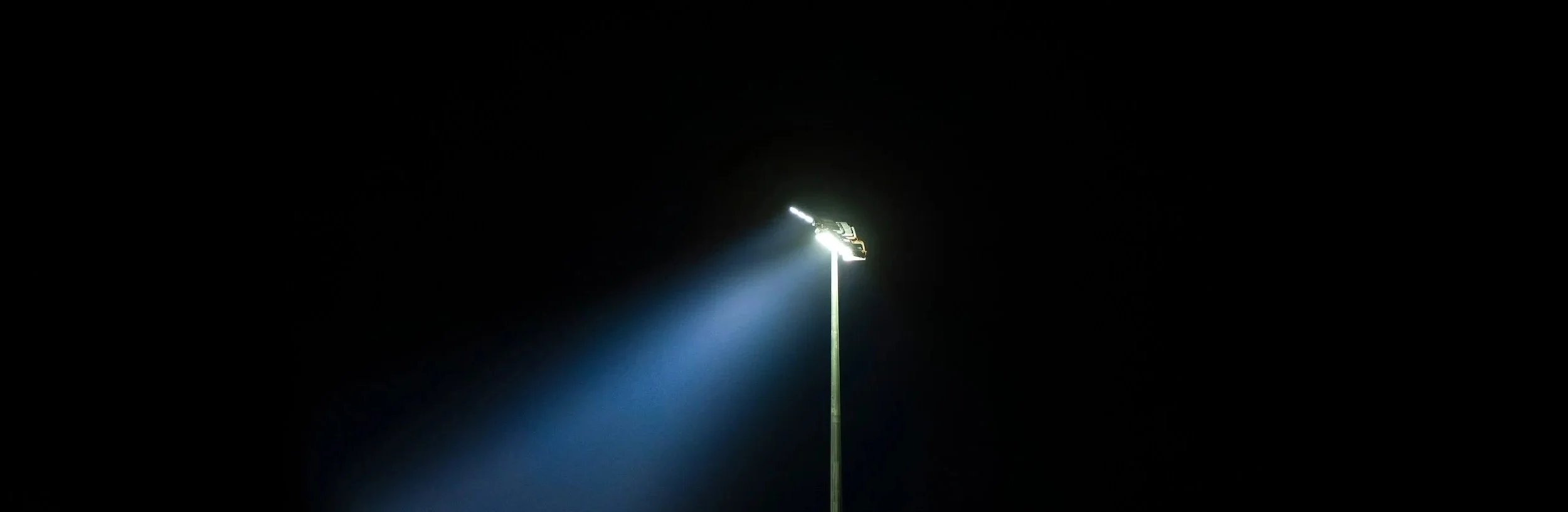 A tall streetlight illuminating a dark night sky with bright lighting at the top.