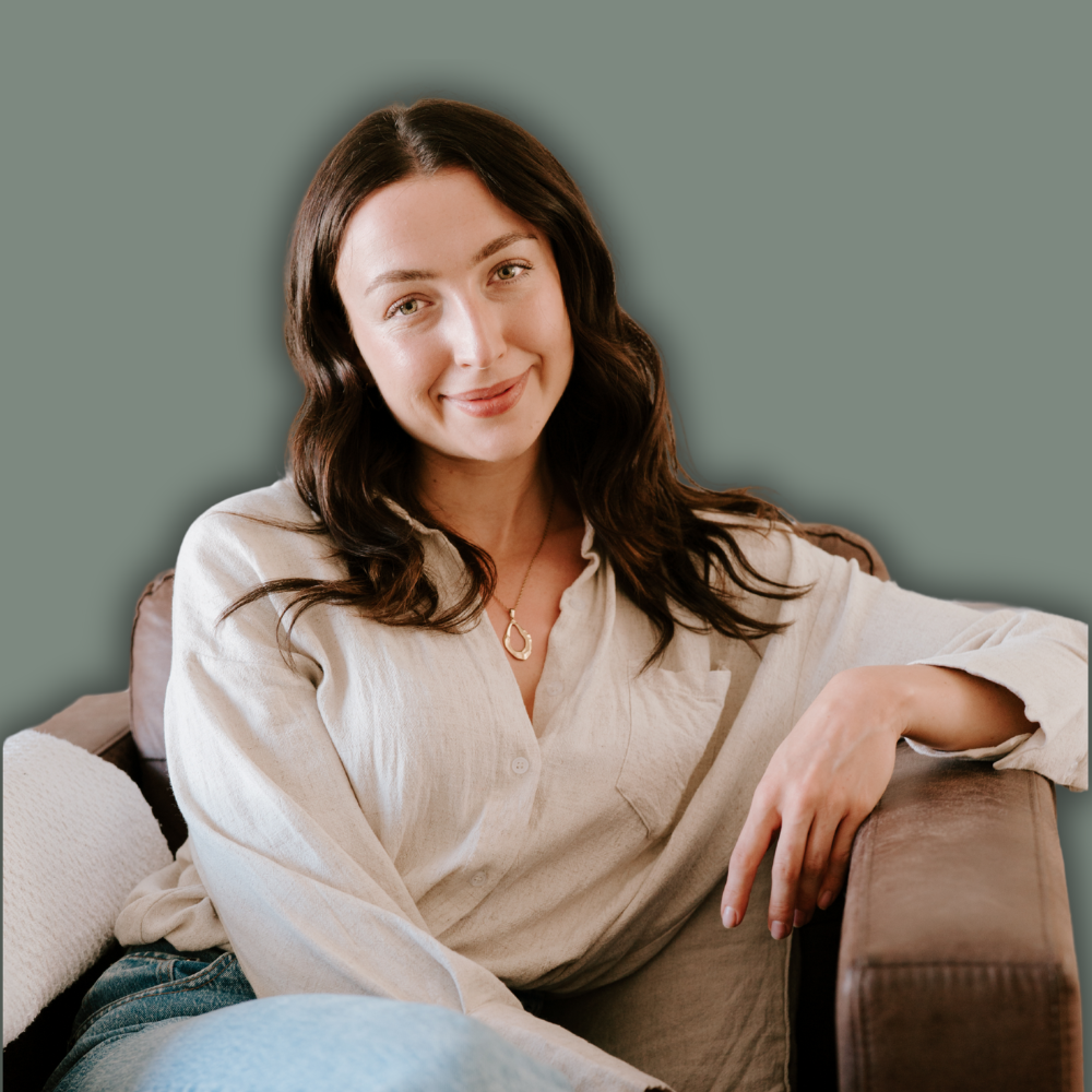 A woman with long dark hair, wearing a beige button-up shirt, sitting on a couch with a relaxed and friendly expression.