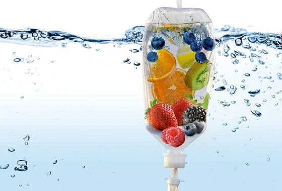 A clear plastic bag filled with various fresh fruits including strawberries, blueberries, raspberries, blackberries, orange slices, kiwi slices, and lemon slices, submerged in water with bubbles and splashes.