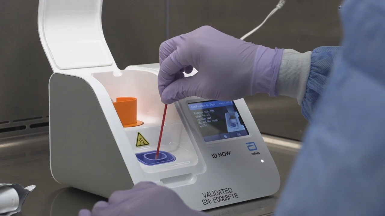 A healthcare worker with purple gloves performing a rapid COVID-19 test using a swab and an automated testing device.