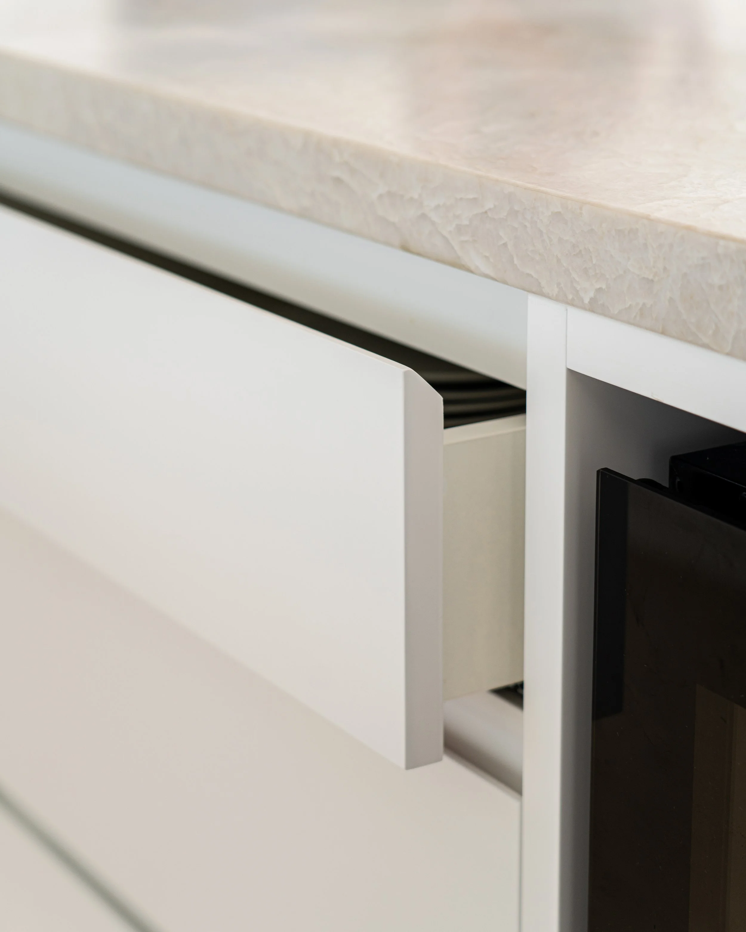 Close-up of a partially open white kitchen drawer beneath a beige marble countertop.