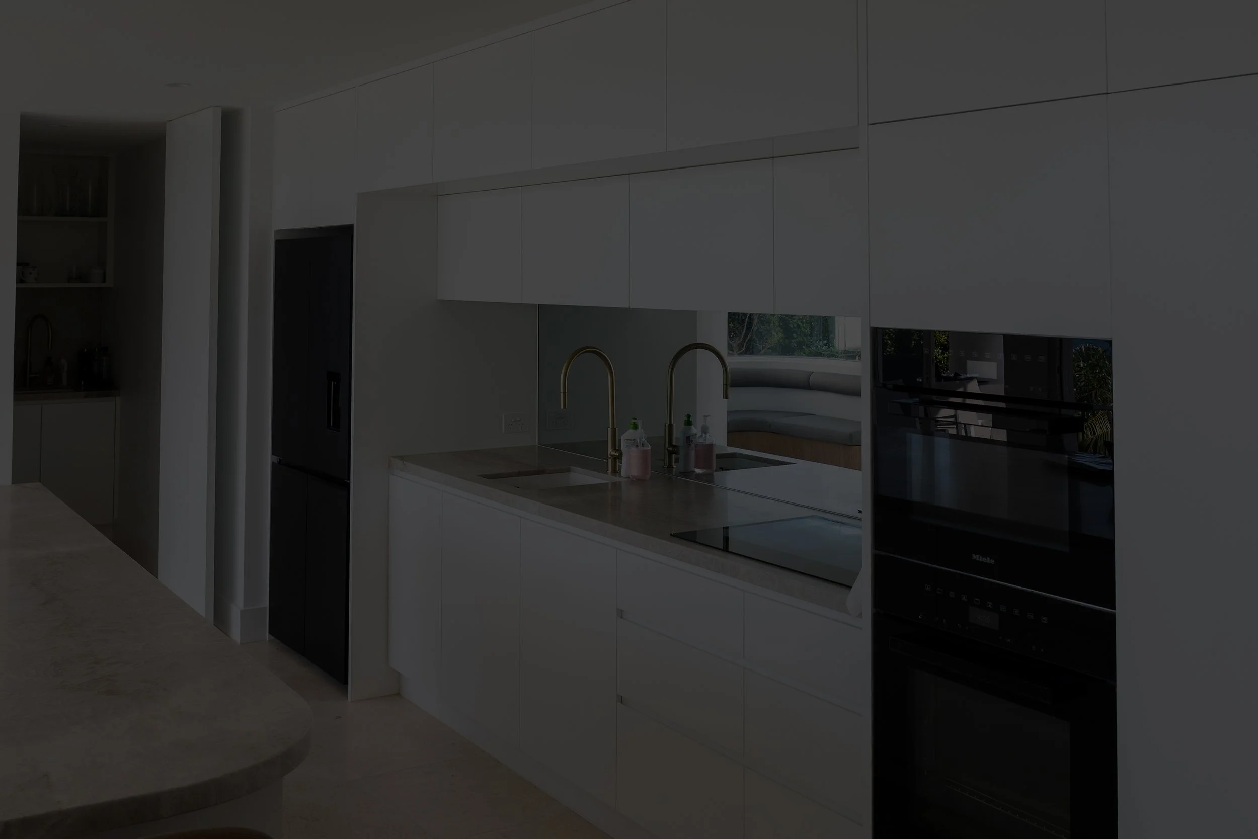 Modern kitchen with white cabinets, double sink with gold faucet, and built-in oven, with some soap and sanitizer bottles next to the sink.