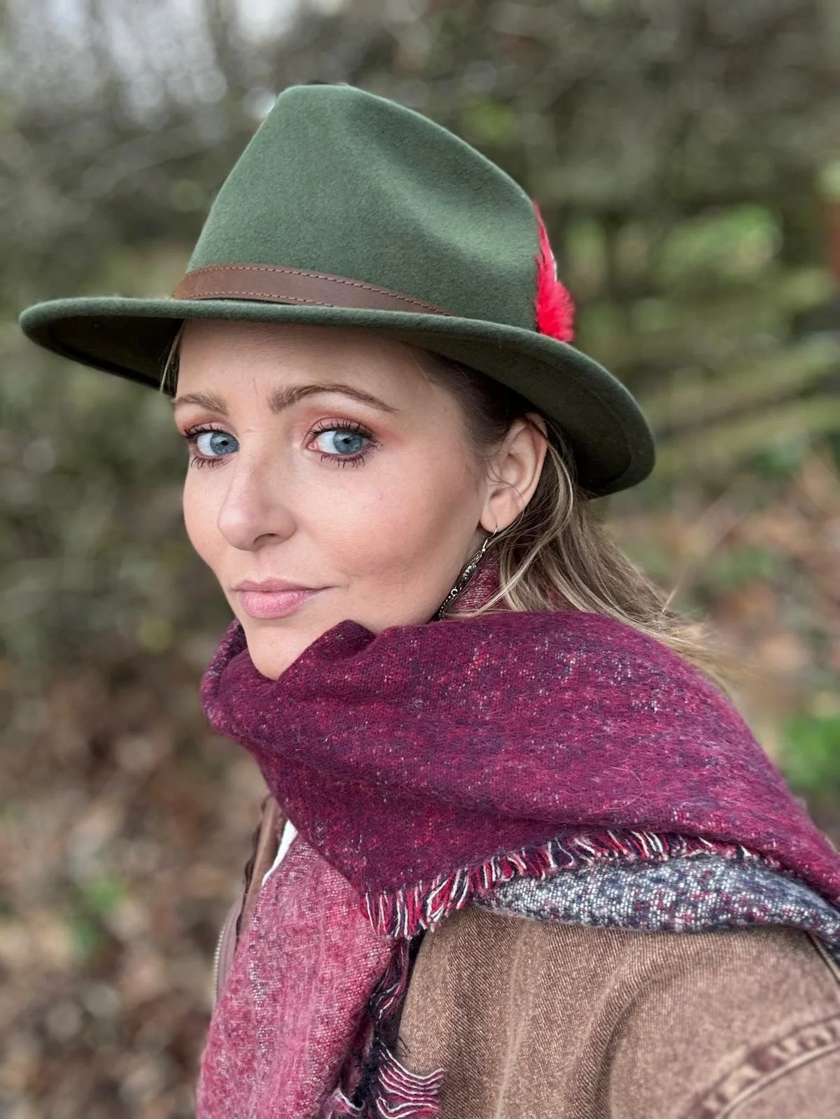 Person wearing green hat with red feather and maroon scarf in outdoor setting