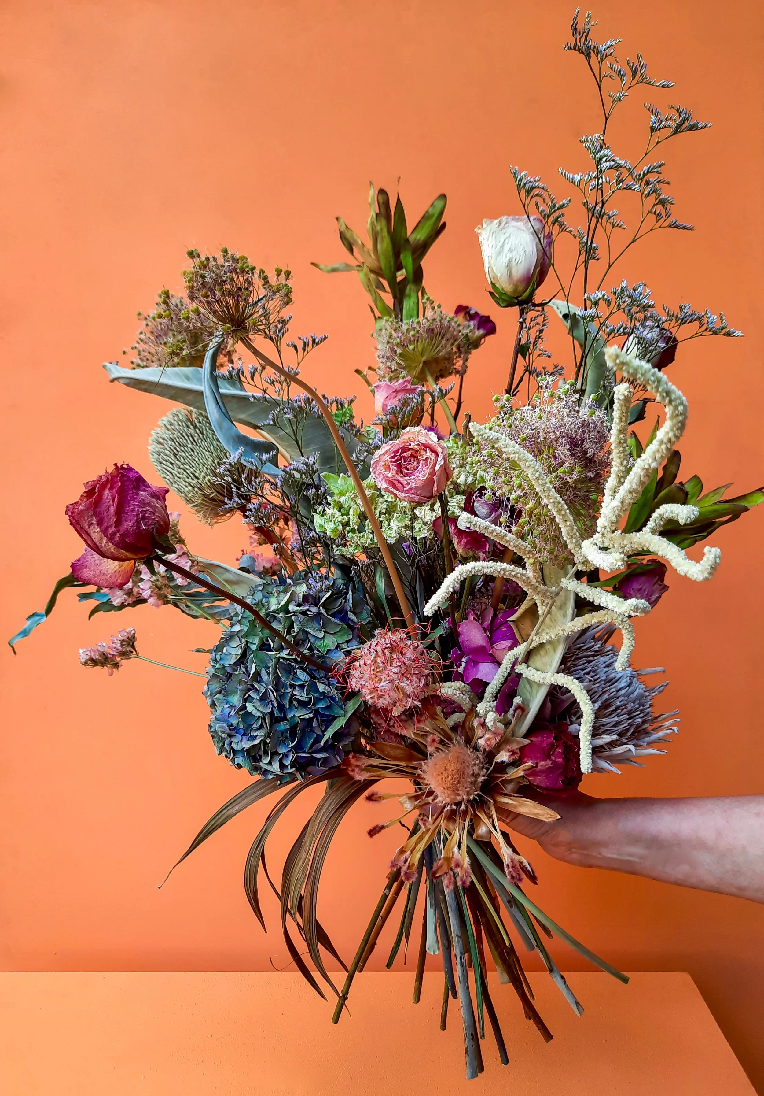 Dried flower arrangement with roses, hydrangea and allium against orange background, Berlin