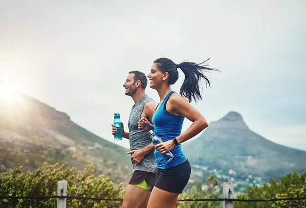 A man and a woman jogging outdoors in a scenic mountainous area, both smiling and carrying water bottles.