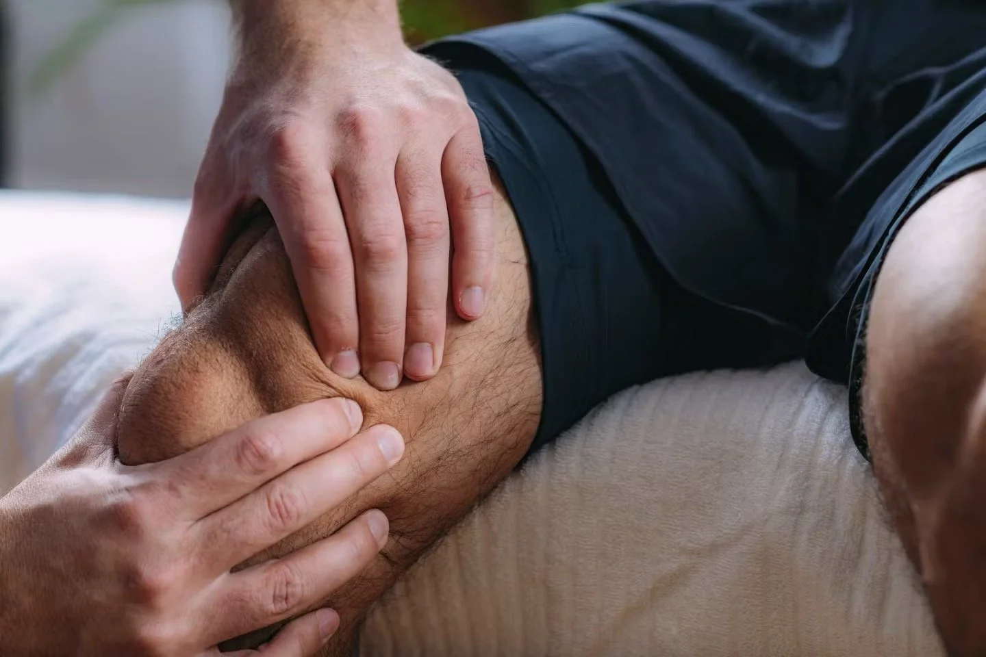 Close-up of a person receiving a massage on their thigh, laying on a cushioned surface.