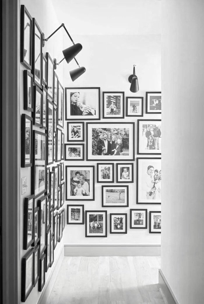 Black and white photo of a gallery wall with various framed photographs of people and outdoor scenes.