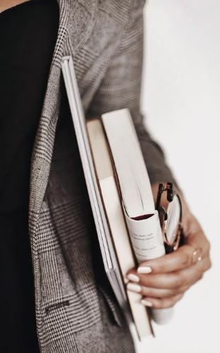 Person holding books, a pen, and a small tube or lotion container.