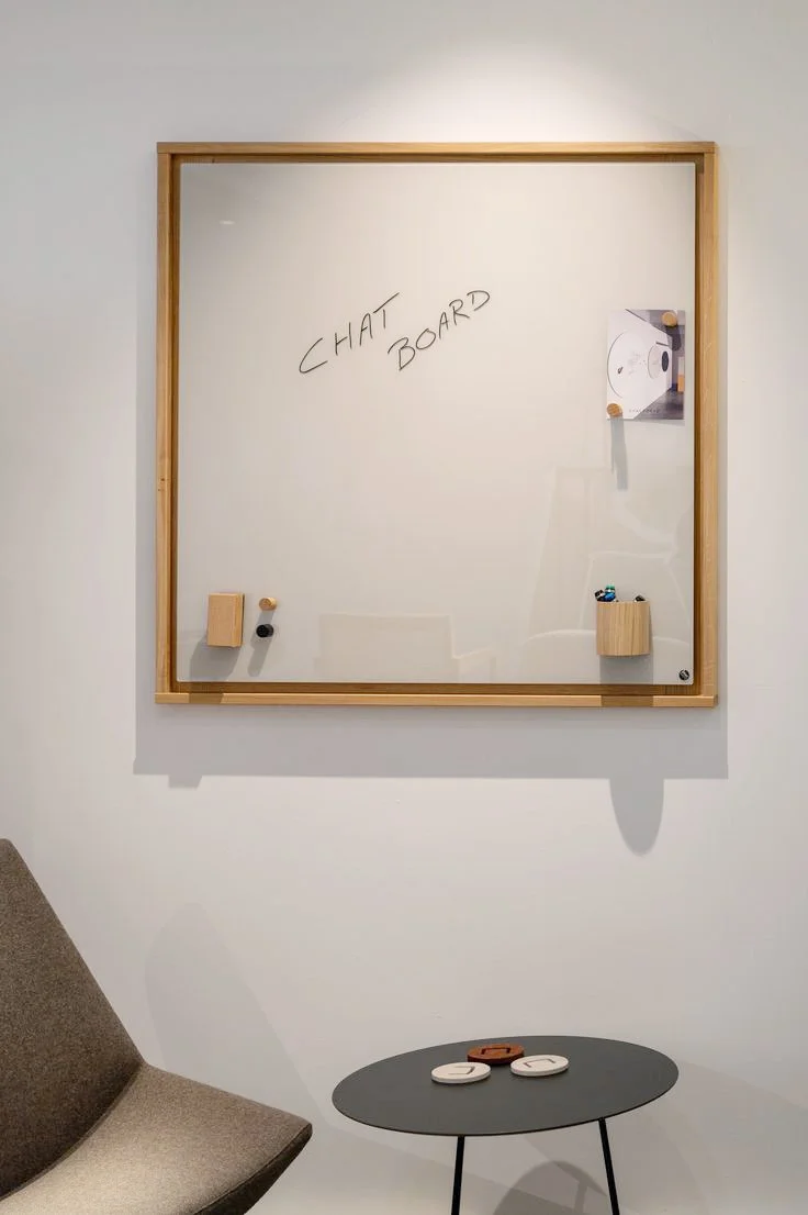 Whiteboard with 'CHAT BOARD' written on it, two small containers holding markers, and a picture of a turntable, with a small round table and a chair nearby.