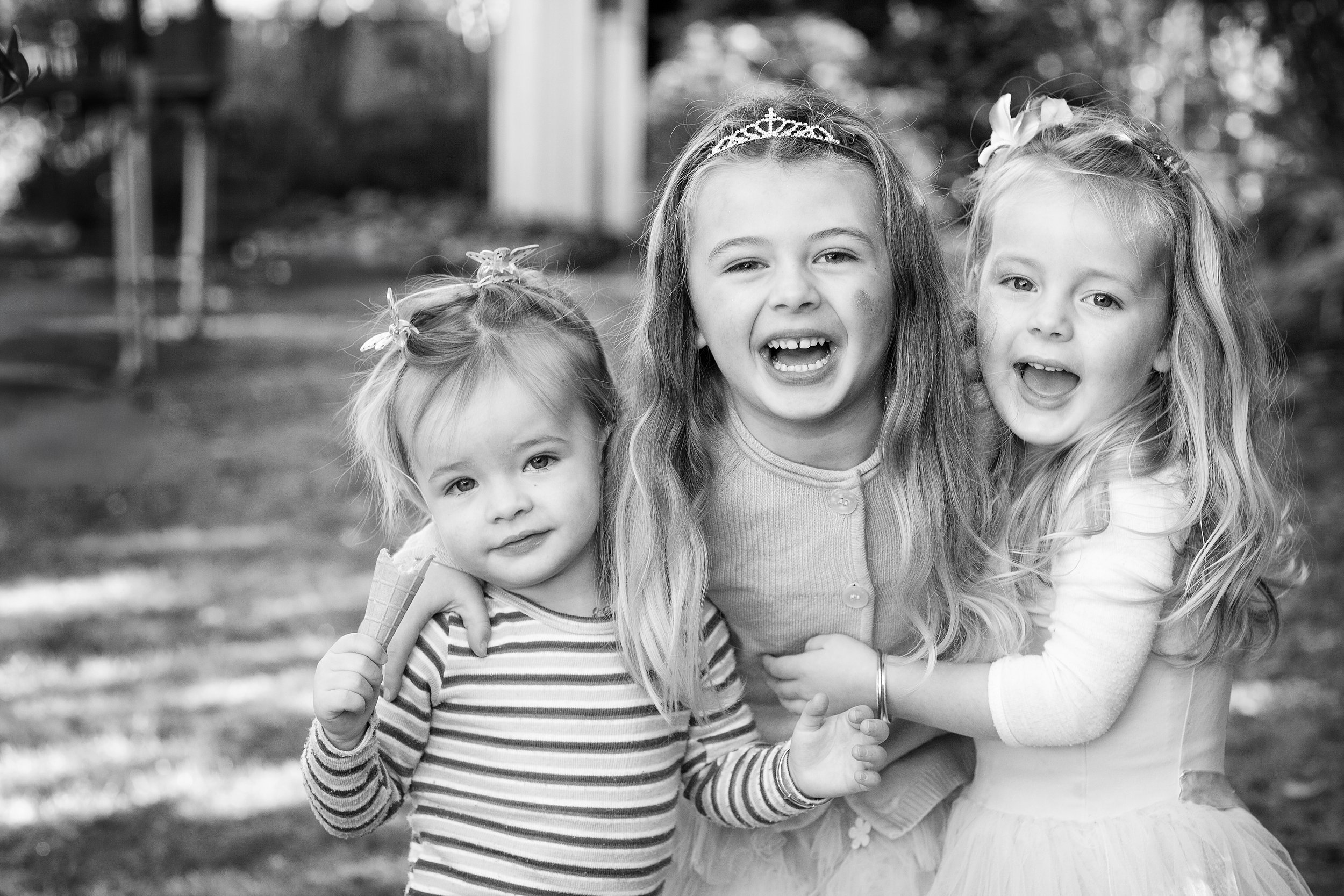 Black and white photo of three young girls smiling and posing outdoors, with the youngest holding an ice cream cone.