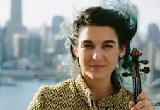 Woman holding a violin with a city skyline in the background.