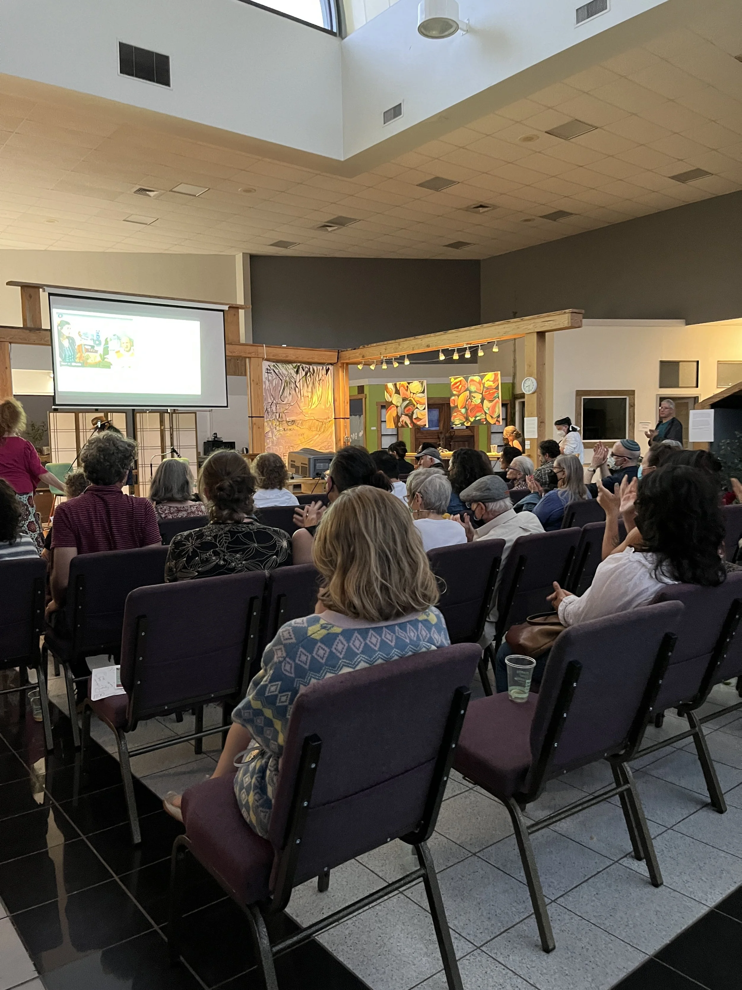 People seated in a conference room watching a presentation on a large screen.